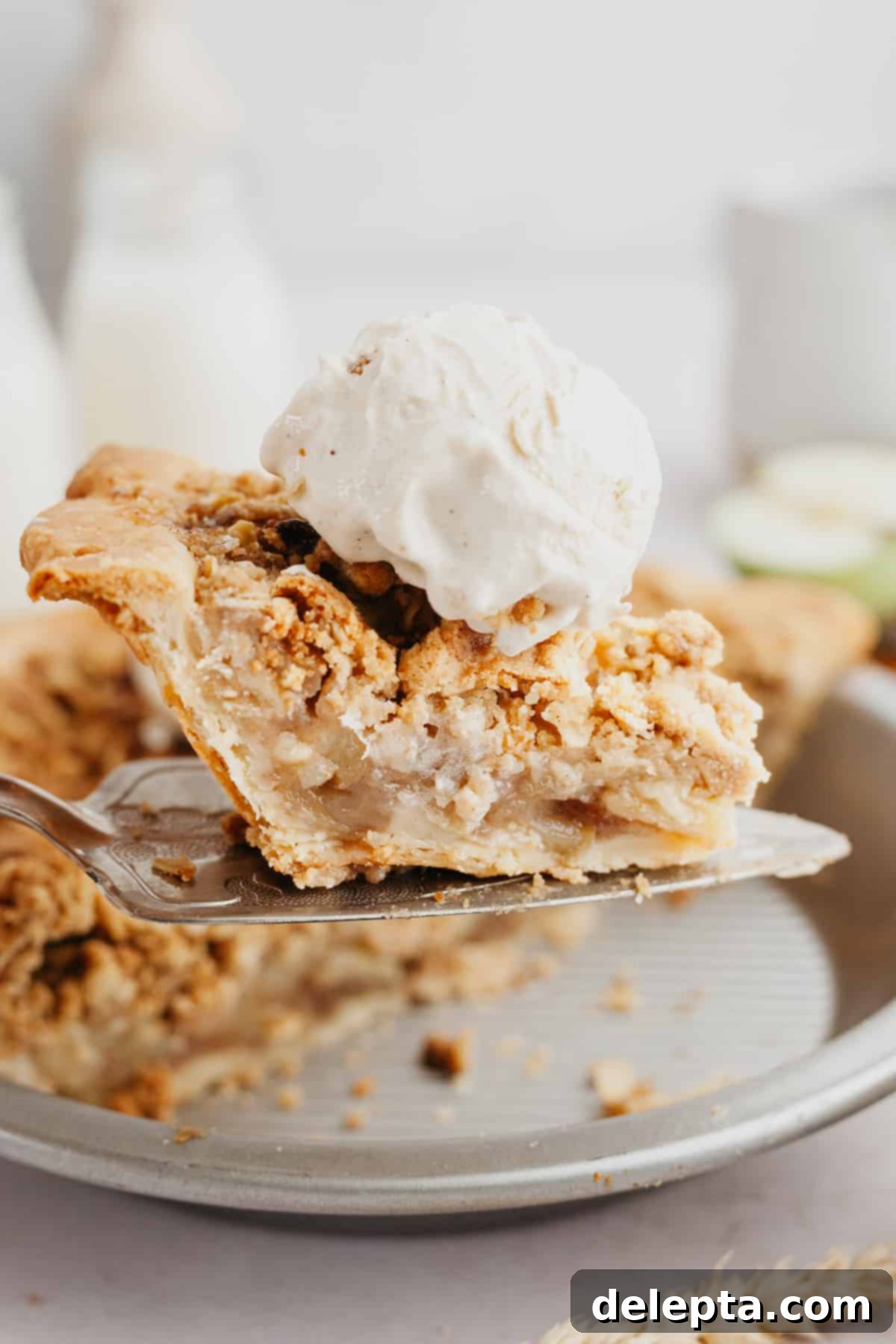 Rustic Oat Topped Apple Pie 8 A delectable slice of apple oat crumble pie, adorned with a scoop of creamy vanilla ice cream, ready to be enjoyed.