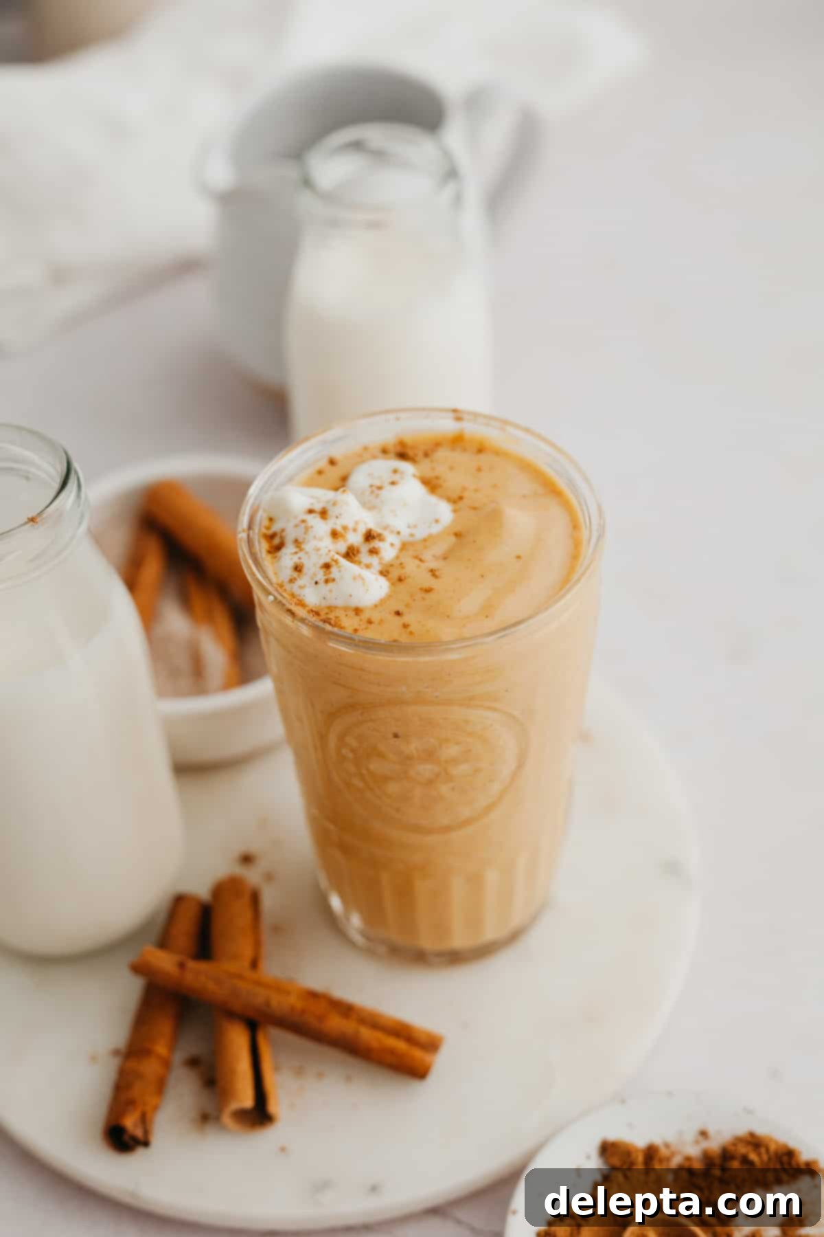 Creamy Banana Pumpkin Pie Smoothie 2 A vibrant orange pumpkin pie smoothie, garnished with a sprinkle of pumpkin pie spice, in a tall, clear glass, set against a rustic autumn background.