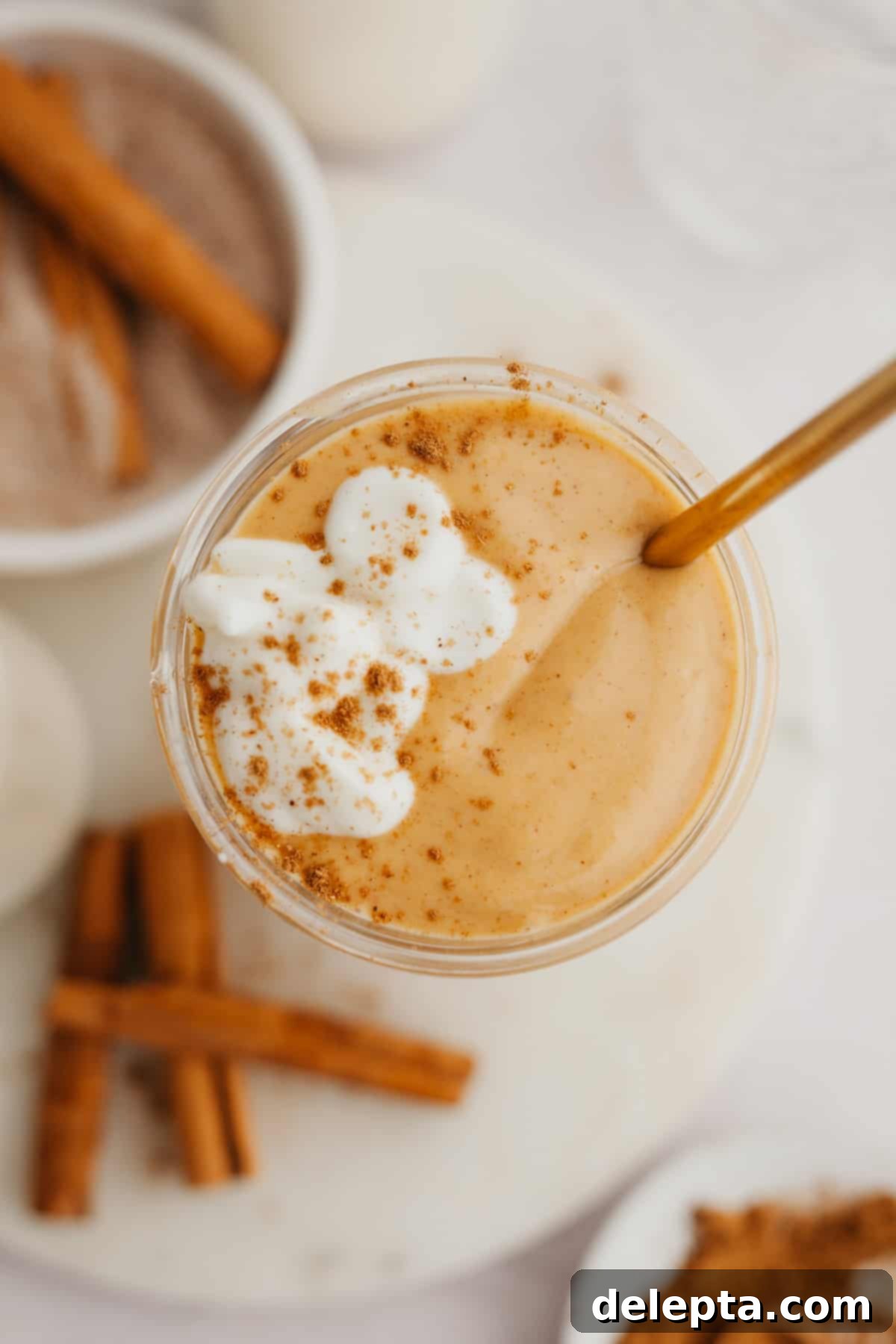 Creamy Banana Pumpkin Pie Smoothie 5 A refreshing pumpkin smoothie in a large, condensation-covered glass, garnished with a sprinkle of cinnamon and a small spoon, showcasing its rich, autumnal color.