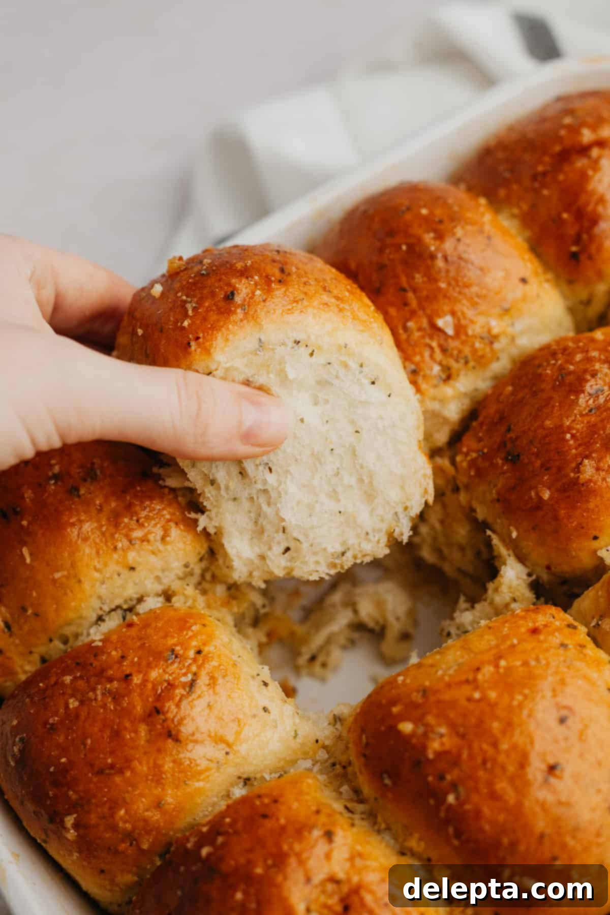 Irresistibly Soft and Fluffy Garlic Dinner Rolls 9 Close-up of baked garlic dinner rolls in a white baking dish, glistening with herb butter and flaky sea salt.