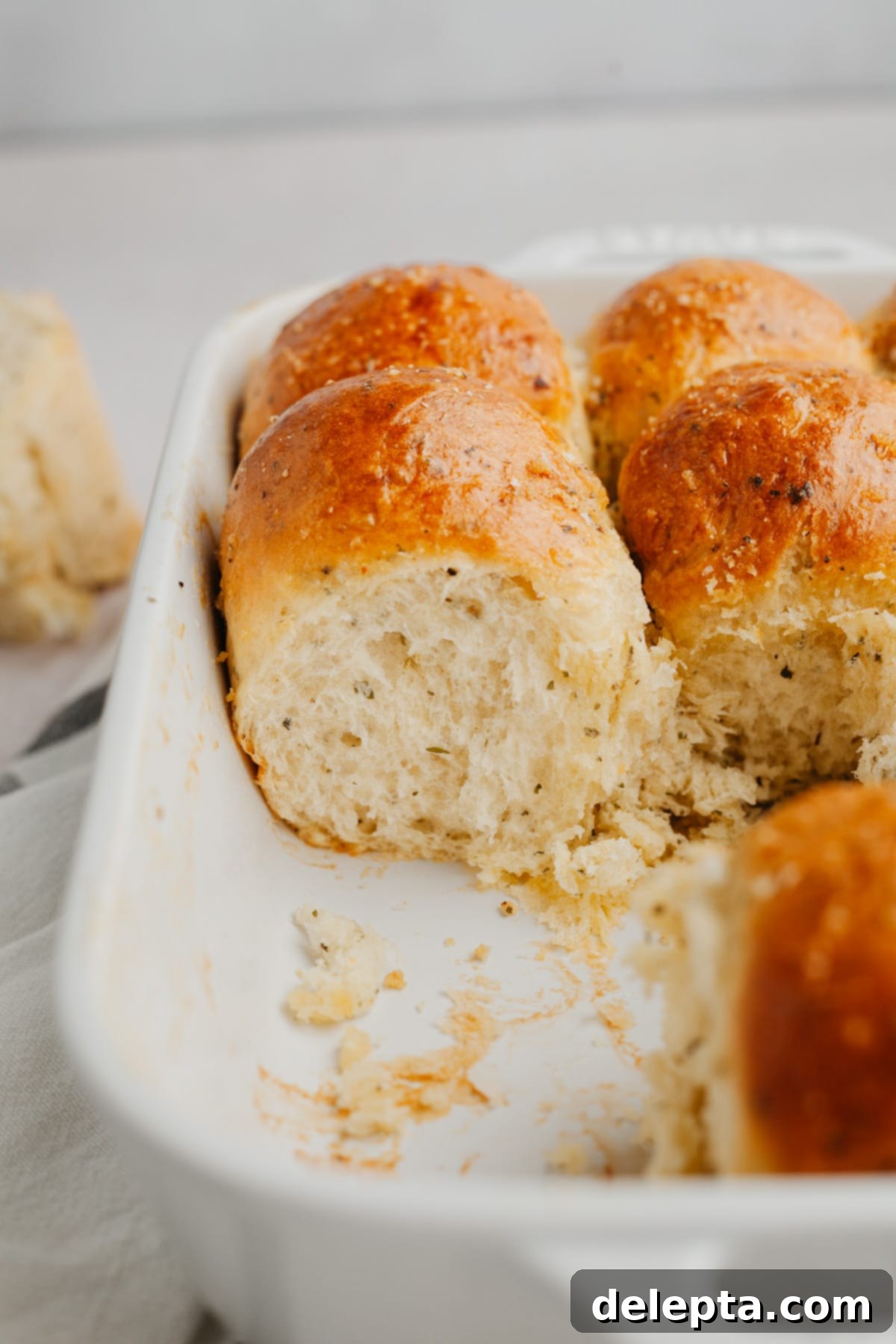 Irresistibly Soft and Fluffy Garlic Dinner Rolls 10 A stack of three golden brown garlic dinner rolls on a beige linen.
