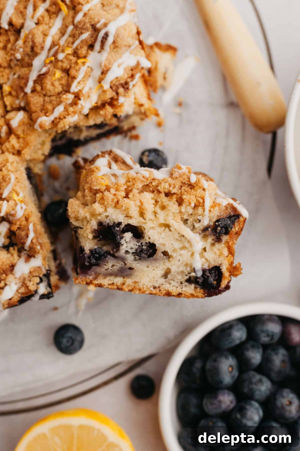 Pratik ve Enfes Yaban Mersinli Limonlu Kahve Keki 10 A close-up shot of a perfectly sliced piece of lemon blueberry coffee cake with a rich crumb topping, revealing the moist interior and scattered blueberries.