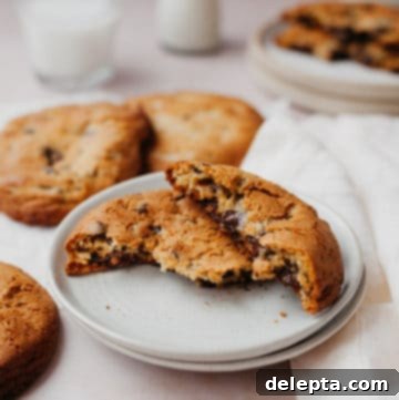 Halva Chocolate Chip Cookie Giants 11 A close-up of a stack of freshly baked, thick halva chocolate chip cookies on a white plate, showing their golden crust and enticing texture.