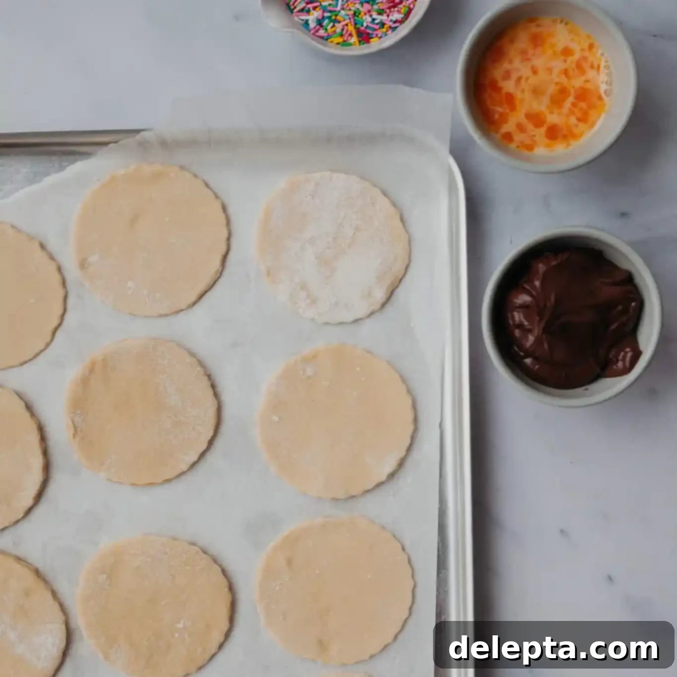 Purim Chocolate Pockets 5 Overhead of hamantaschen dough rounds ready for filling, with small bowls of sprinkles, Nutella, and eggwash