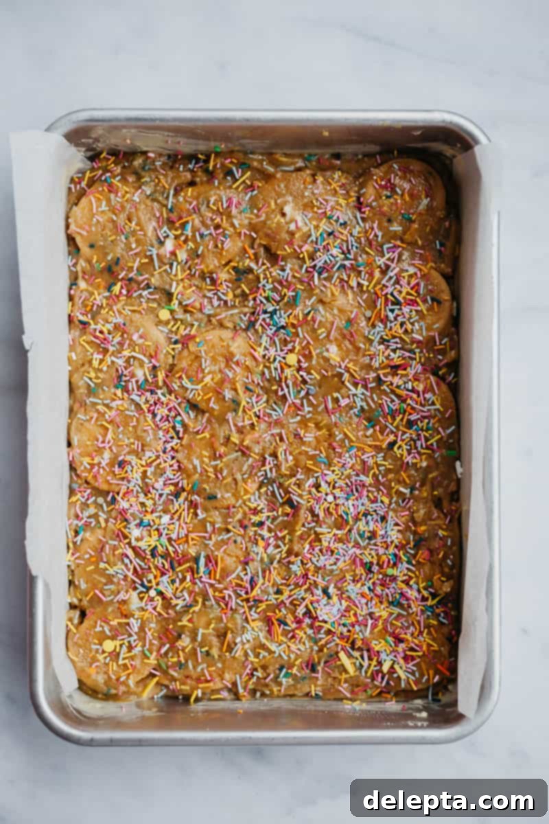 Sprinkle-Studded Golden Oreo Gooey Bars 11 Unbaked funfetti bars in a baking tray, with the second layer of batter covering the golden Oreos and topped with extra sprinkles, ready for the oven.