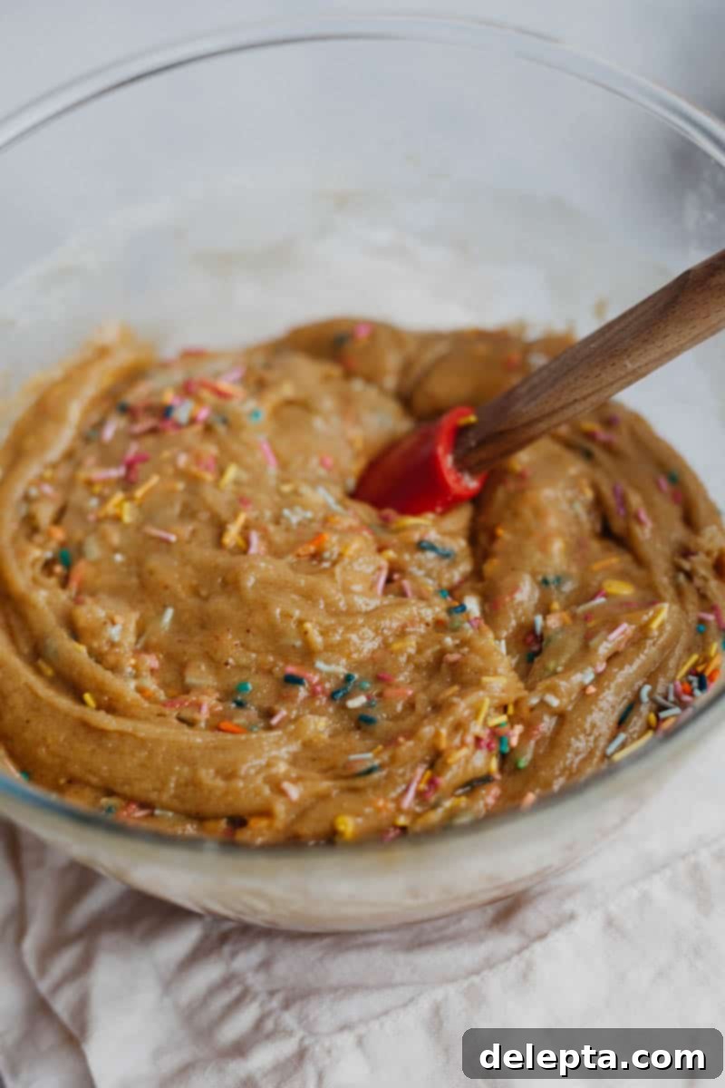 Sprinkle-Studded Golden Oreo Gooey Bars 8 Blondie batter in a clear pyrex bowl with colorful long strand sprinkles folded in, ready for baking.