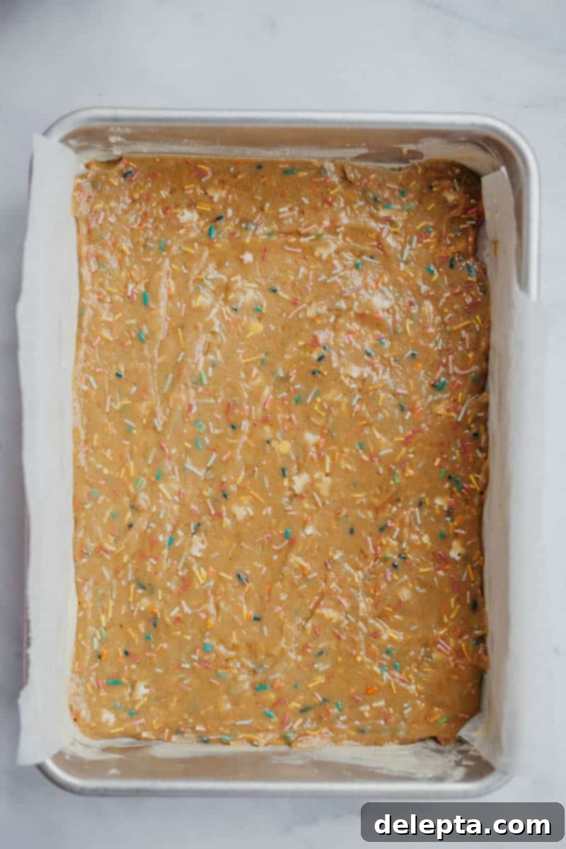 Sprinkle-Studded Golden Oreo Gooey Bars 9 First layer of funfetti blondie batter spread in a parchment-lined baking tray, before adding the Oreos.