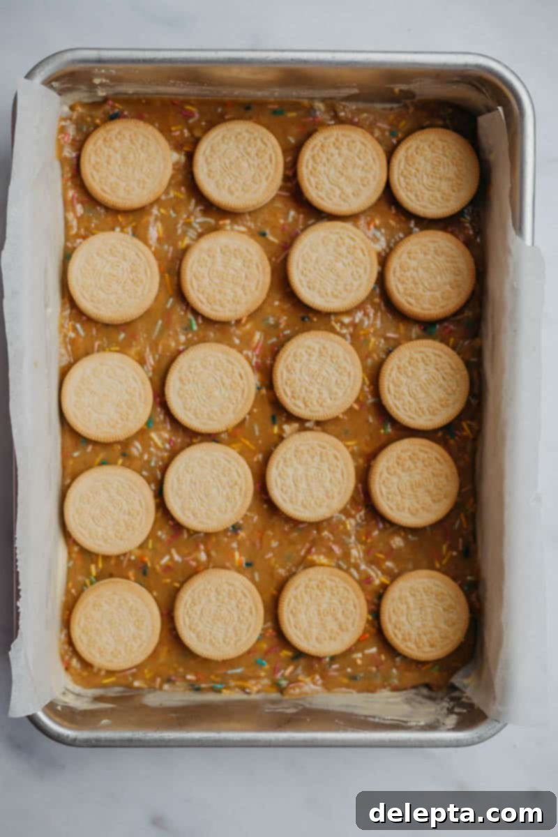 Sprinkle-Studded Golden Oreo Gooey Bars 10 Golden Oreos neatly arranged on the first layer of funfetti blondie batter in a baking tray.