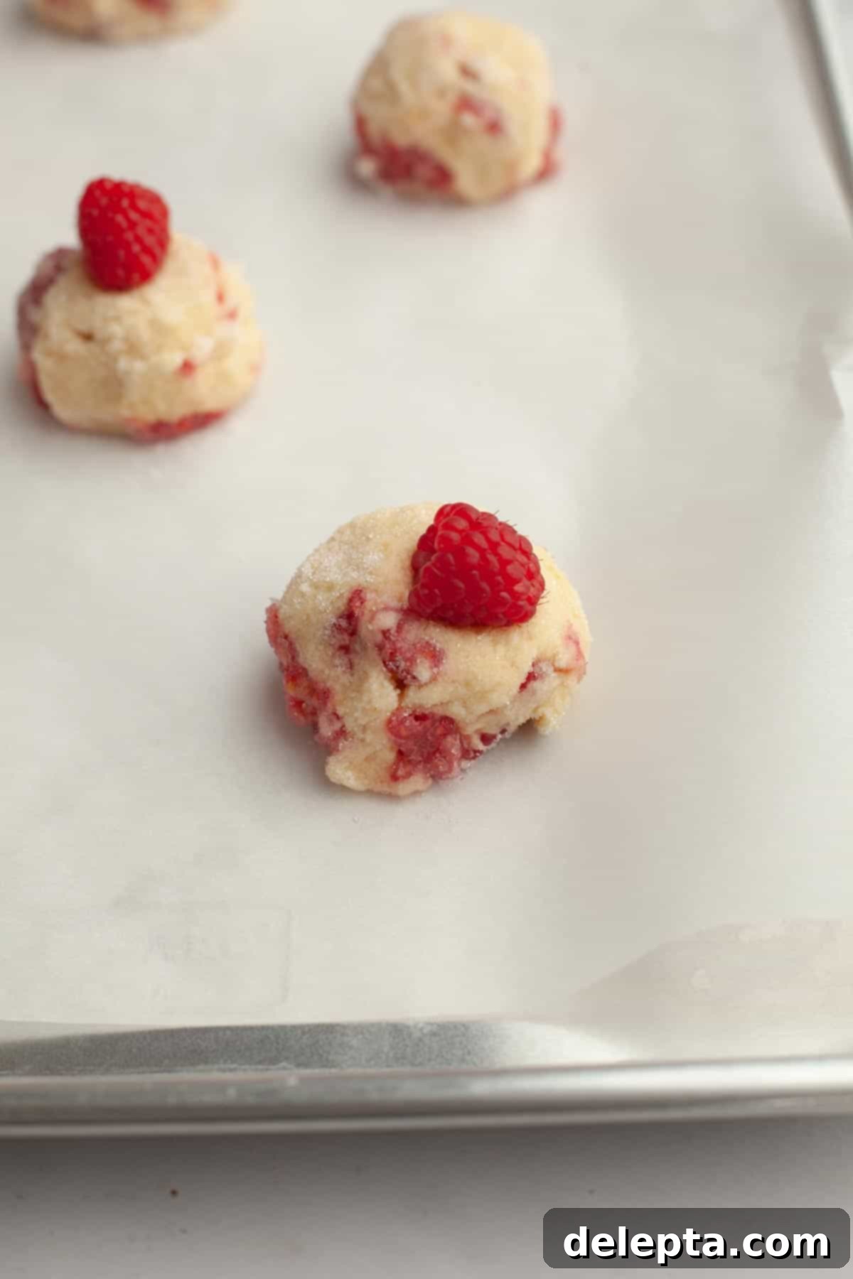 Easy One Bowl Lemon Raspberry Cookies 9 Unbaked lemon raspberry cookies on parchment paper, topped with extra raspberries and sugar.