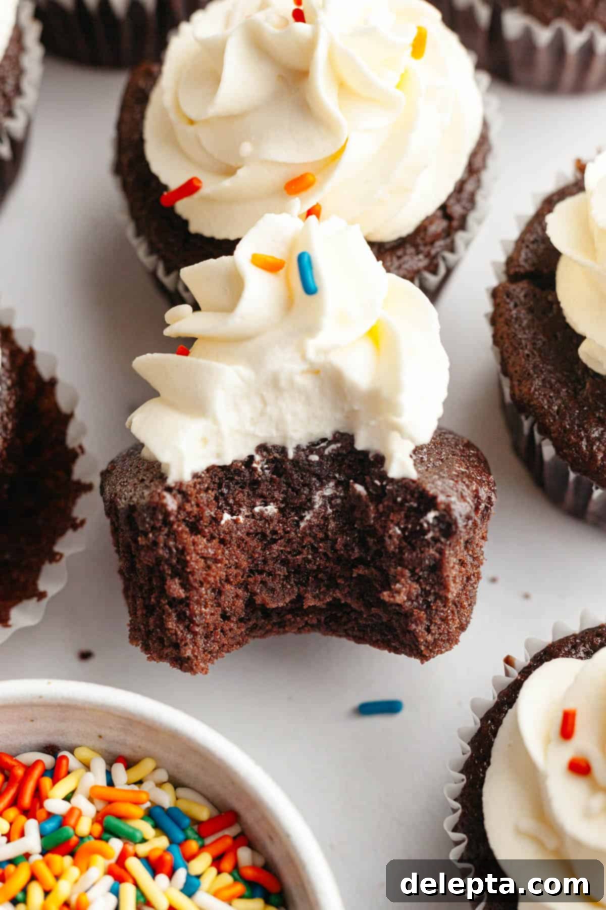Velvet Chocolate Cupcakes with Tangy Cream Cheese Swirl 11 A chocolate cupcake with white frosting and a bite taken out, showing the moist cake inside.