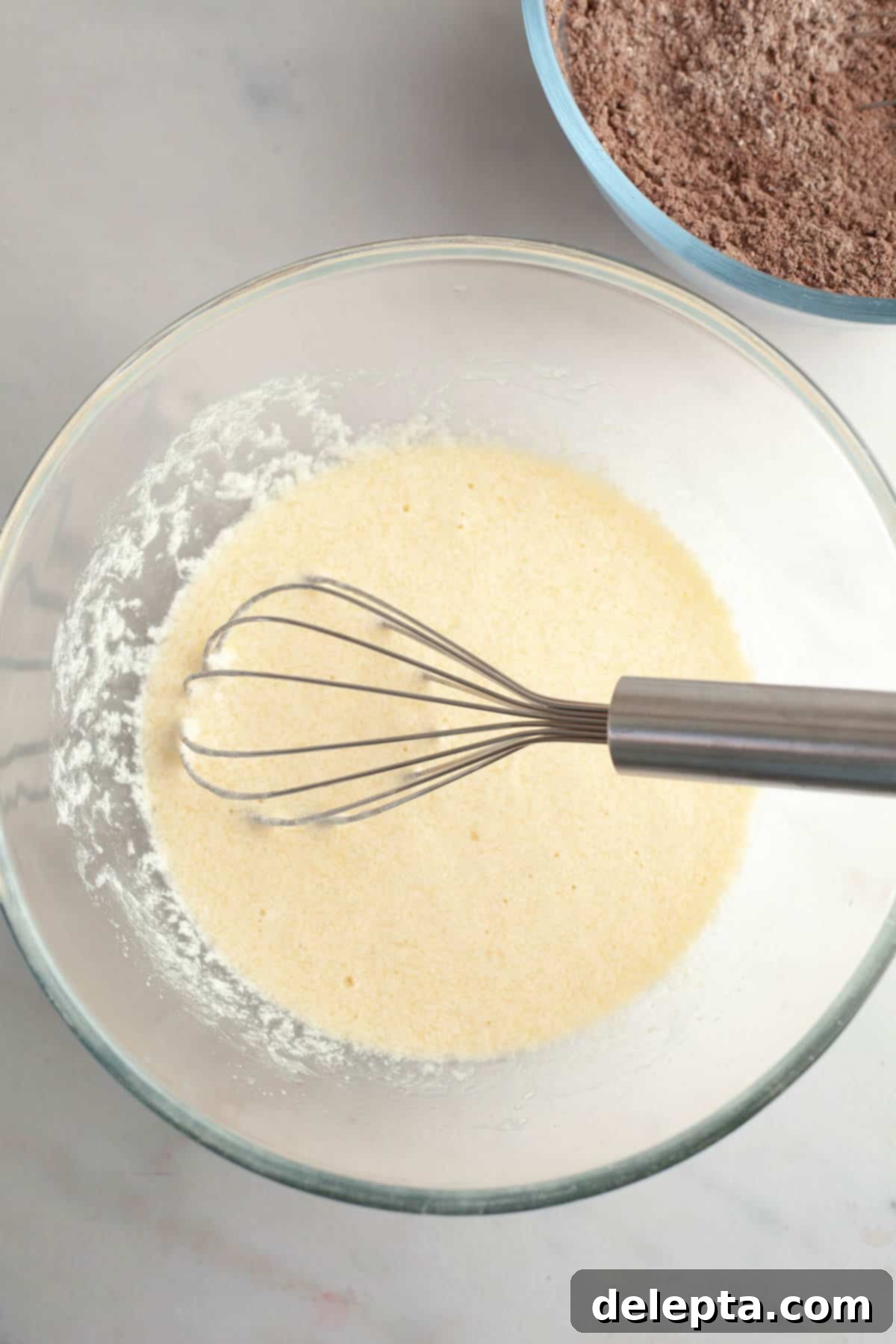 Velvet Chocolate Cupcakes with Tangy Cream Cheese Swirl 5 Whisked pale yellow mixture in a bowl with a whisk, showing wet ingredients combined.