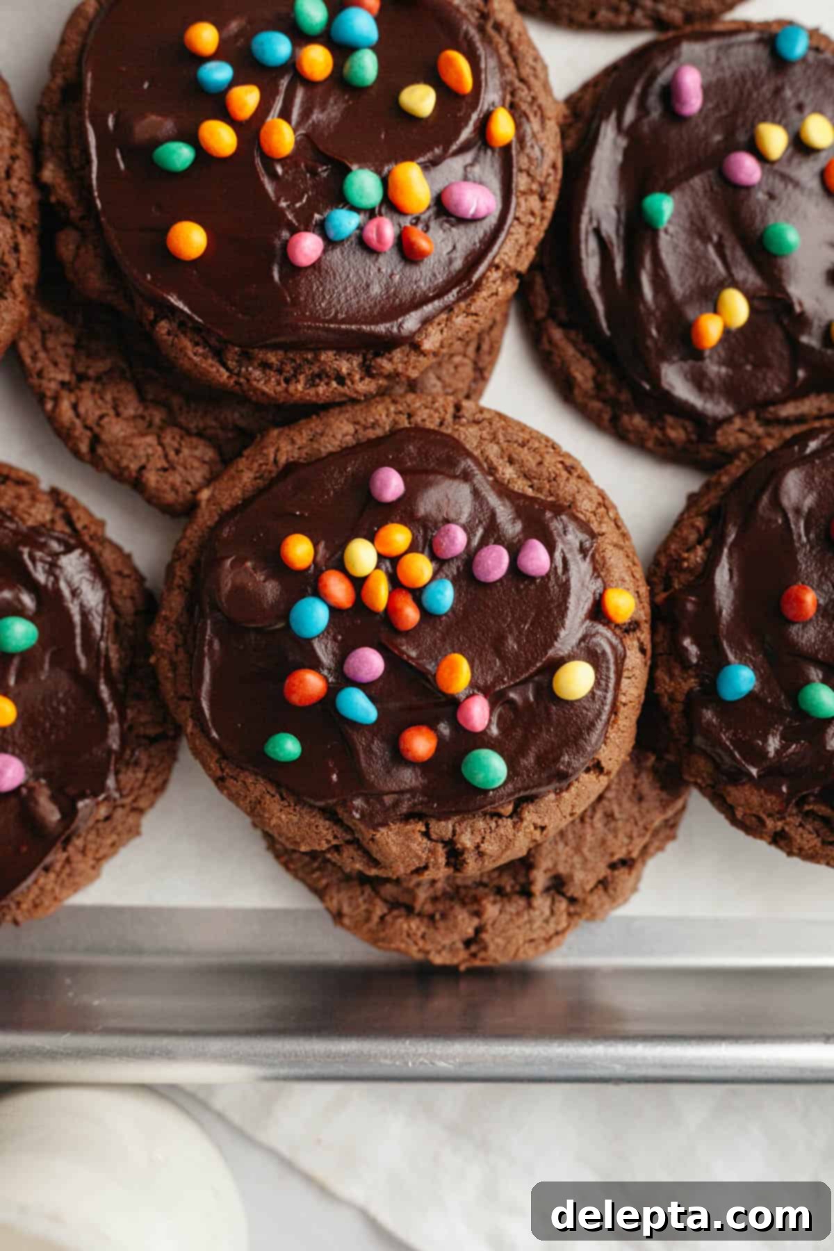Galaxy Brownie Cookies 2 Fudgy chocolate cosmic brownie cookies topped with glossy chocolate ganache and colorful rainbow chips on parchment paper, ready to be enjoyed.