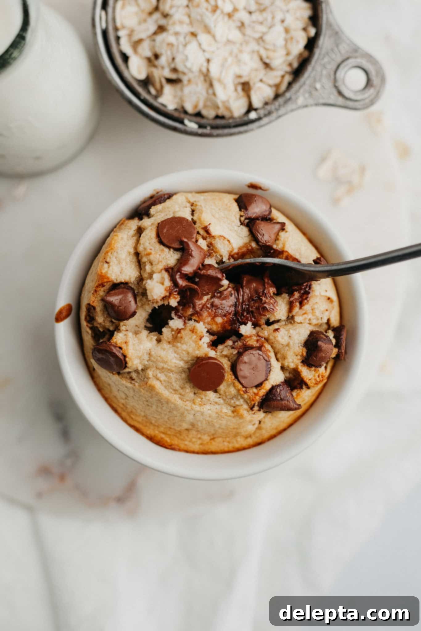 Single-Serve Baked Oat Indulgence 2 A small white ramekin with baked oats, there is a small spoon inside, topped with chocolate chips.
