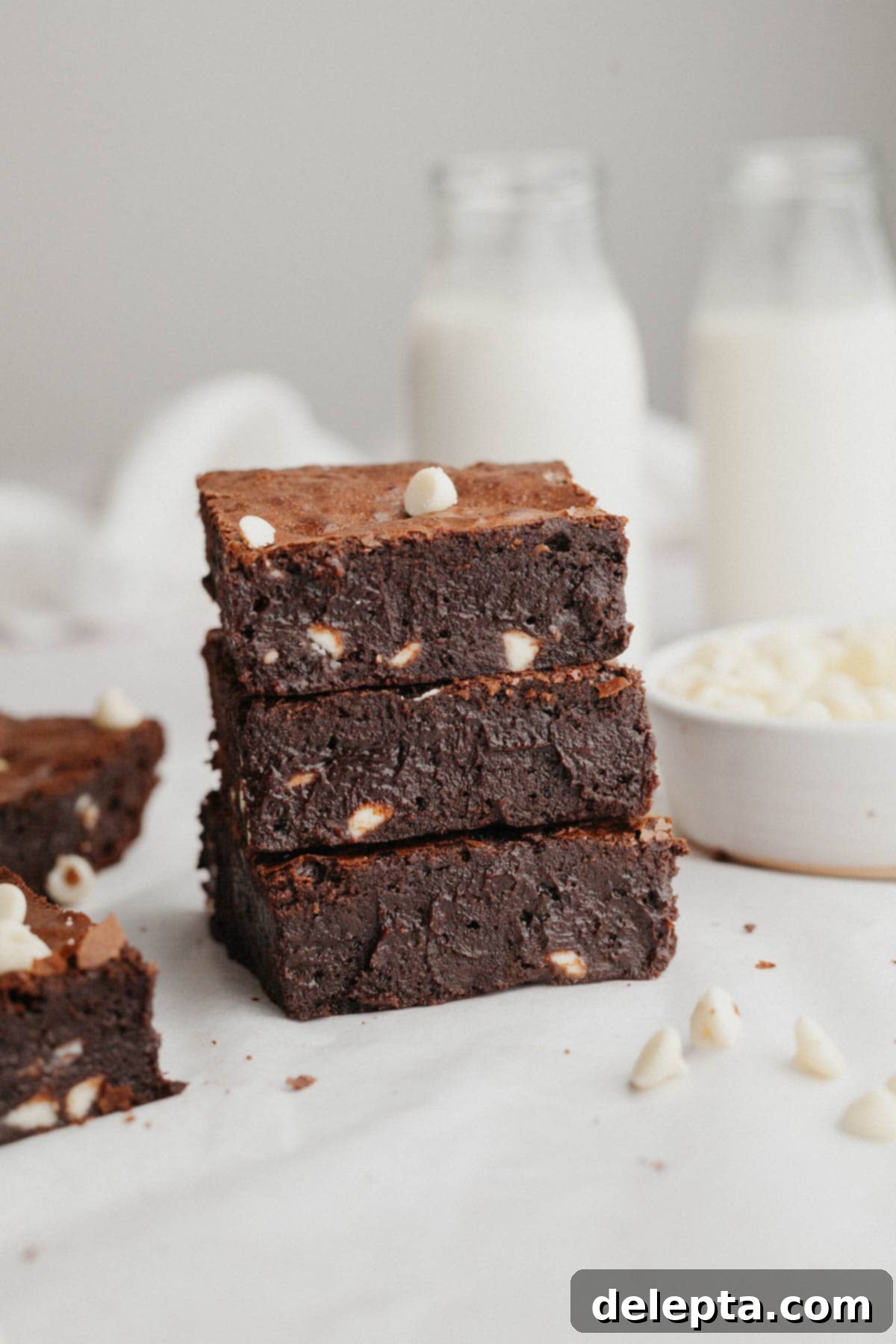 Effortlessly Fudgy White Chocolate Chip Brownies 2 A stack of three incredibly fudgy white chocolate chip brownies, showcasing their rich, dark interior and visible white chocolate chunks.