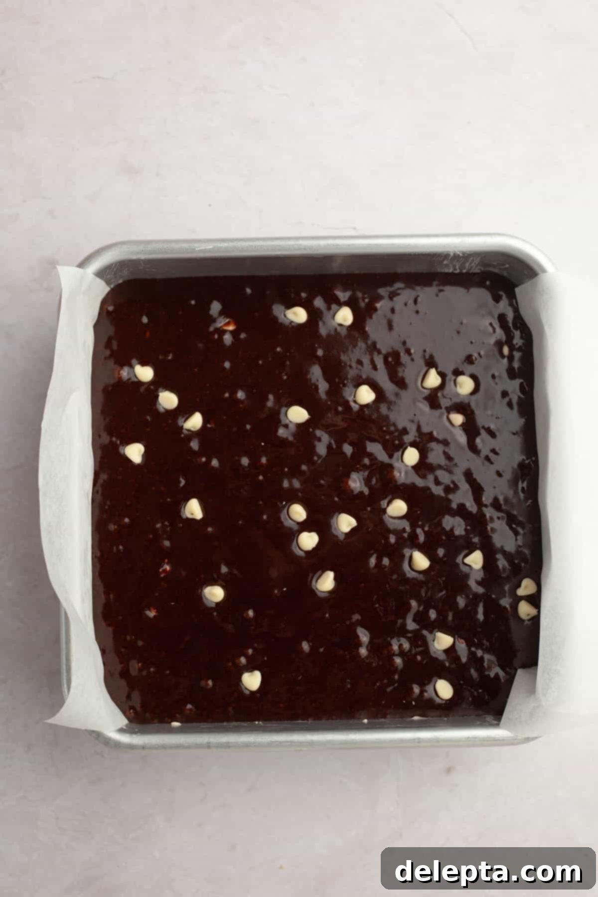 Effortlessly Fudgy White Chocolate Chip Brownies 7 Unbaked brownie batter, sprinkled with extra white chocolate chips, neatly settled in a greased and lined baking pan, ready for the oven.