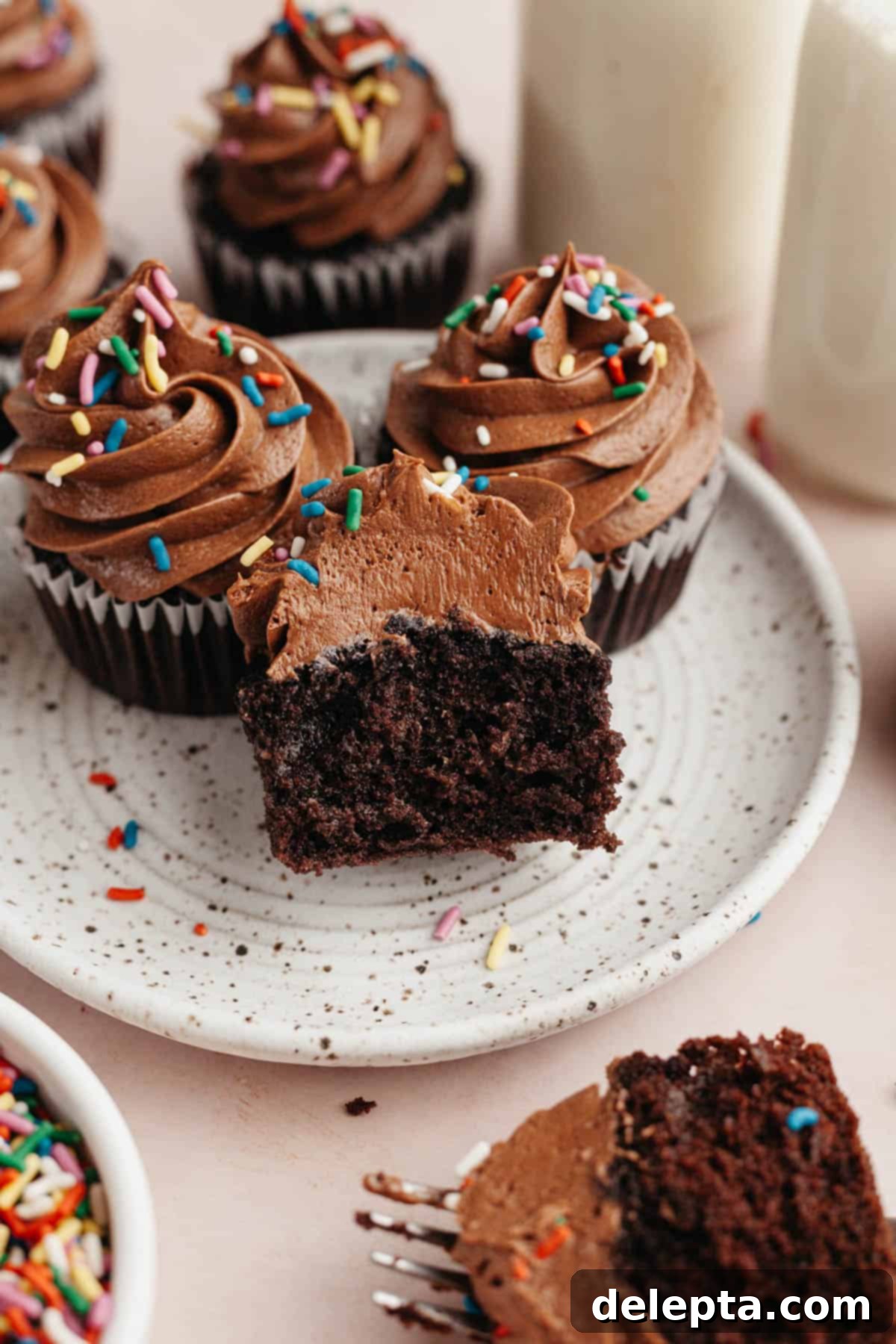 Decadent Chocolate Cream Cheese Cupcakes 10 Three chocolate cupcakes on a plate, one has been cut in half to show the moist crumb.