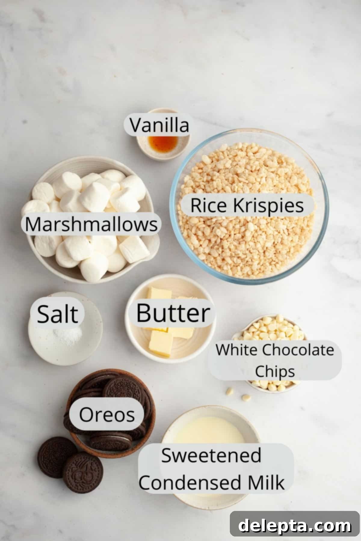 Cookies and Cream Krispie Bars 3 All the essential ingredients neatly arranged in small bowls, ready for making Oreo Rice Krispie Treats: marshmallows, crushed Oreos, Rice Krispies cereal, white chocolate chips, butter, sweetened condensed milk, vanilla extract, and salt.
