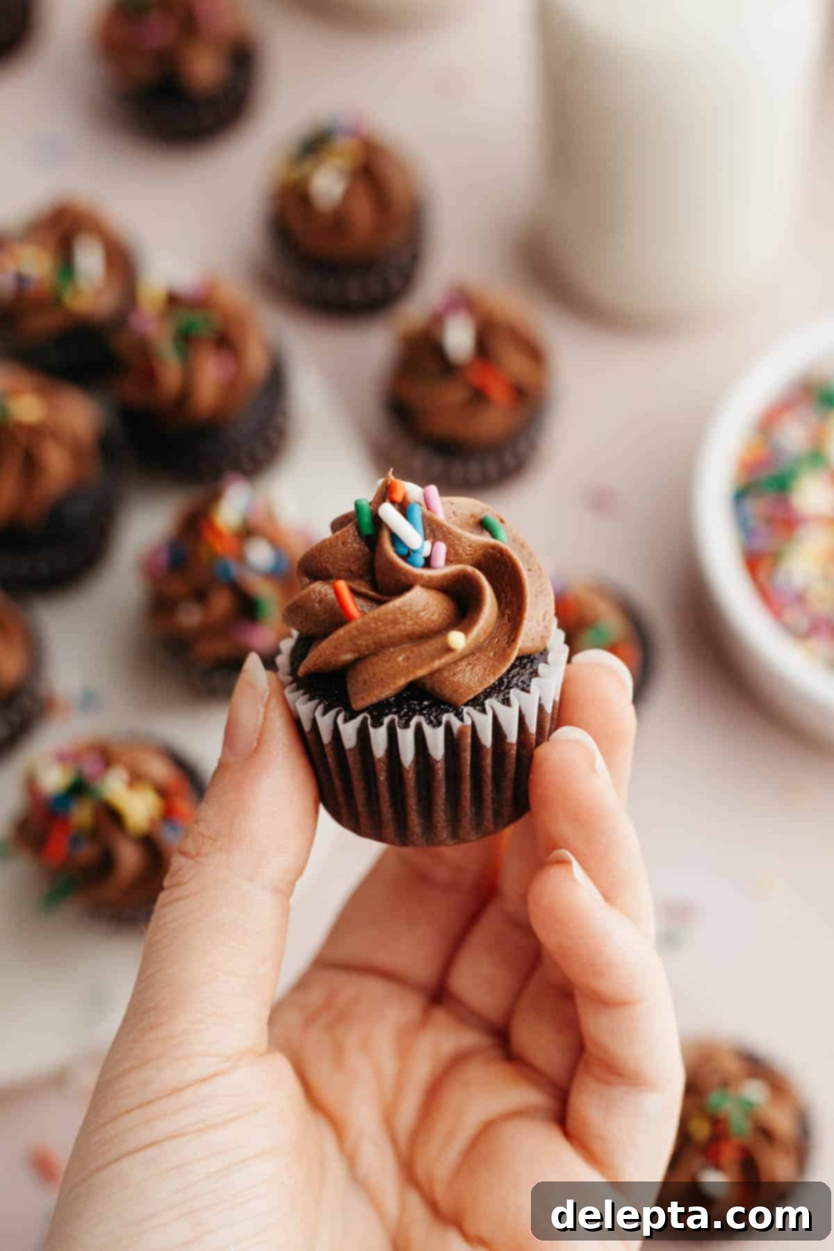 Irresistible Mini Chocolate Cupcakes: Effortlessly Moist Perfection 10 A hand holding a mini chocolate cupcake with chocolate frosting.