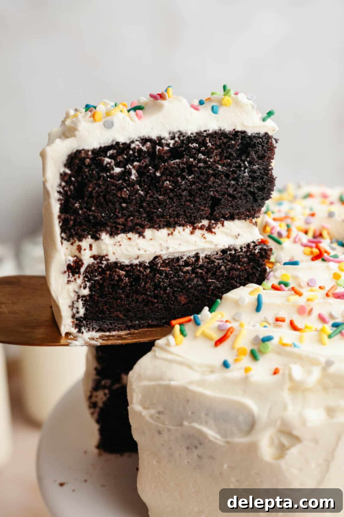 Foolproof Chocolate Cake with Sweet Vanilla Frosting 2 A slice of chocolate cake with vanilla frosting being lifted up with a cake server. The cake is moist and the frosting is smooth.