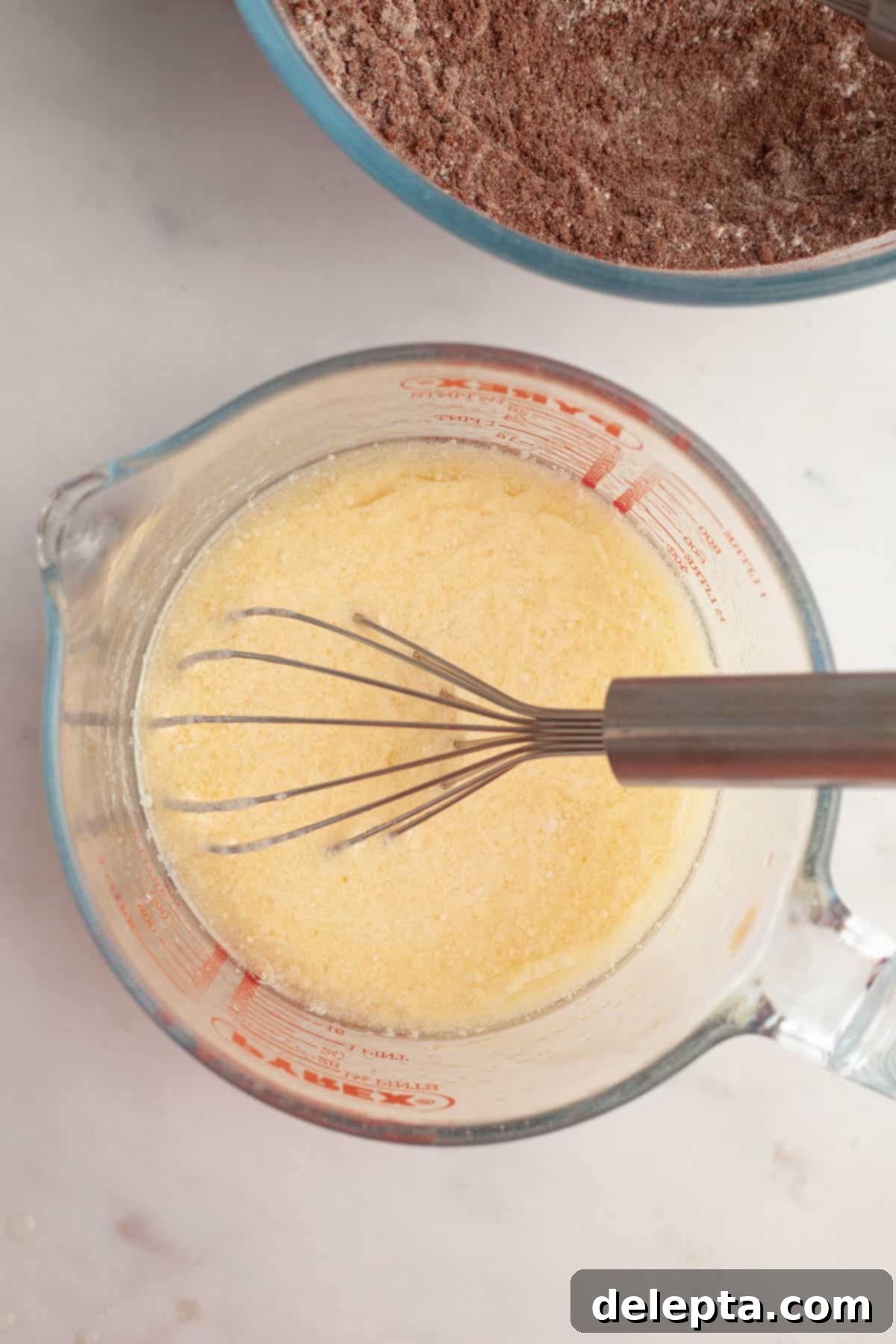 Foolproof Chocolate Cake with Sweet Vanilla Frosting 5 A large glass jug with a whisk and a yellow mixture in it, representing the wet ingredients.