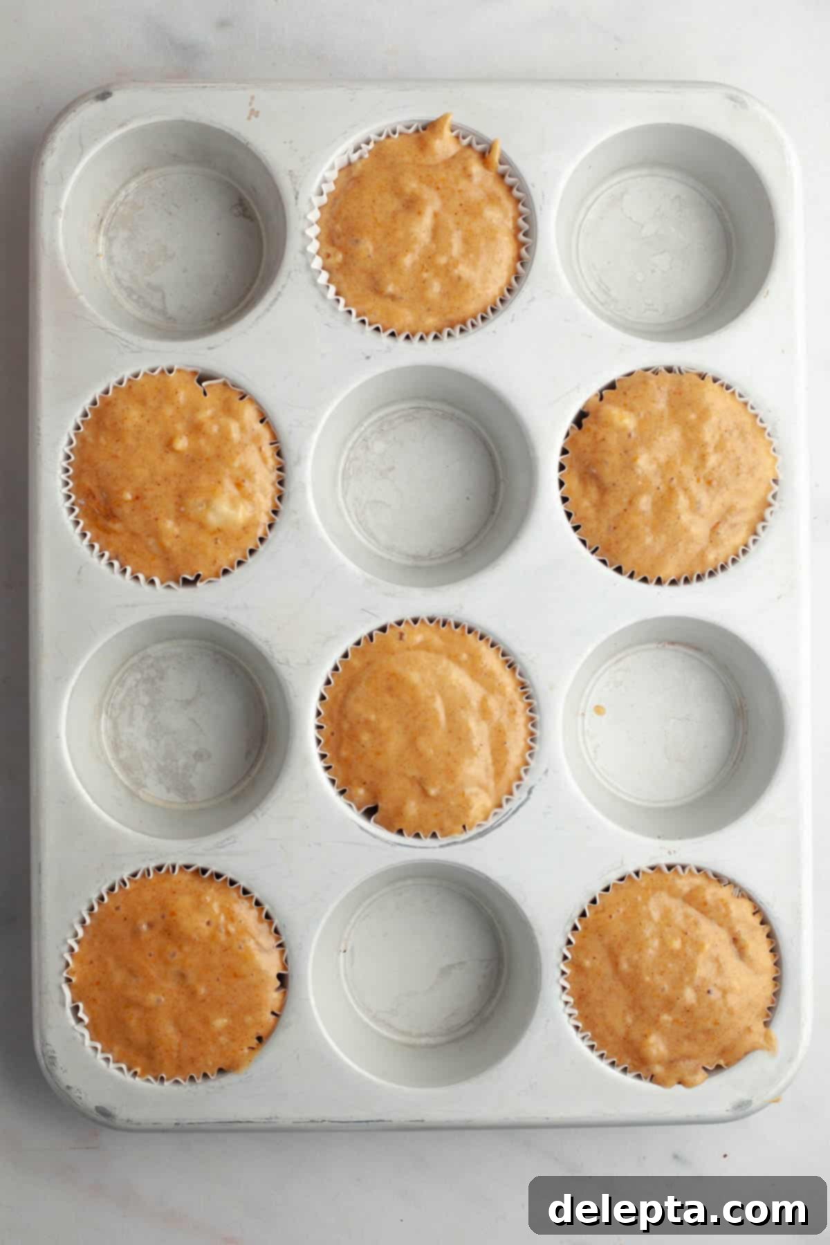 Effortlessly Moist Pumpkin Banana Muffins 6 Unbaked pumpkin banana muffins in a muffin pan.
