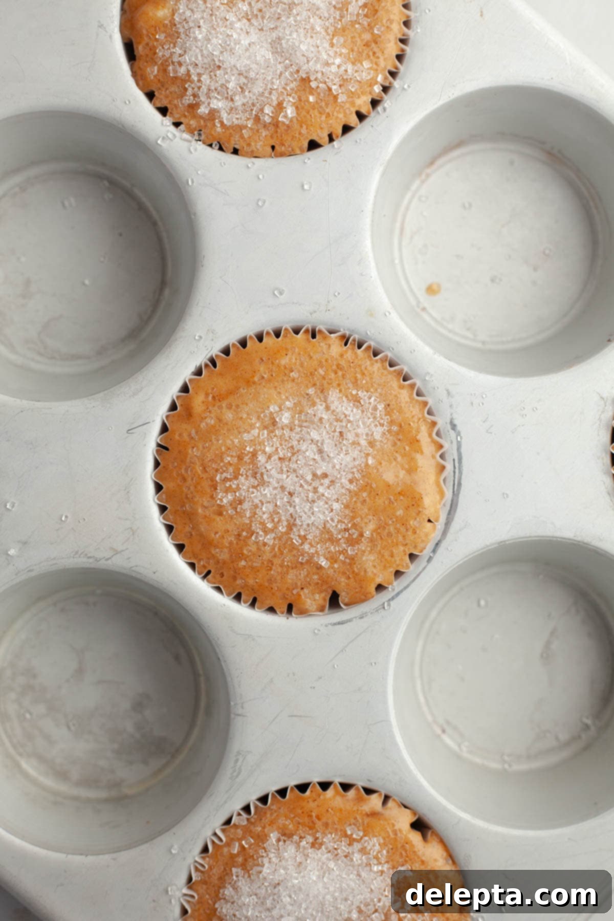 Effortlessly Moist Pumpkin Banana Muffins 7 A close up of unbaked pumpkin banana muffins sprinkled with sparkling sugar.