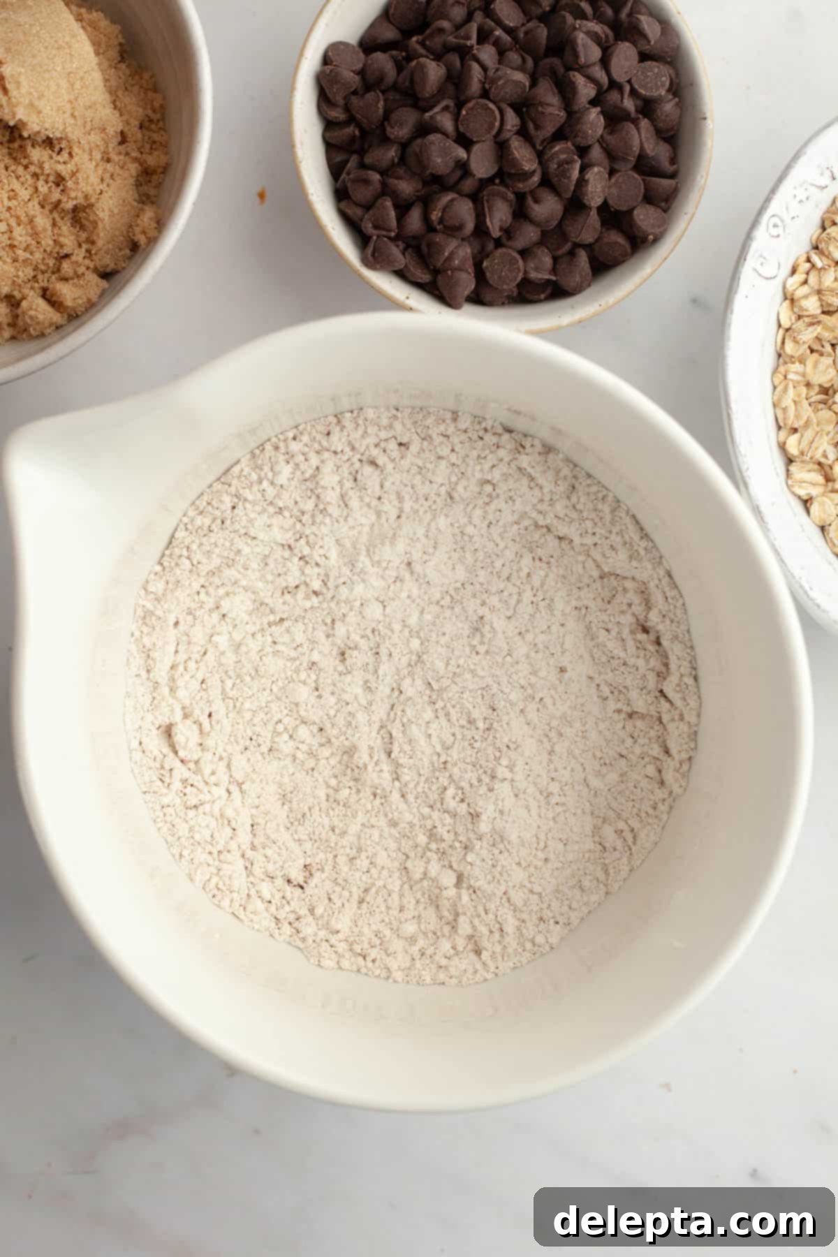 Irresistible Chewy Brown Butter Oatmeal Chocolate Chip Cookies 5 A large white bowl with all-purpose flour, spices, baking soda, and salt mixed together.