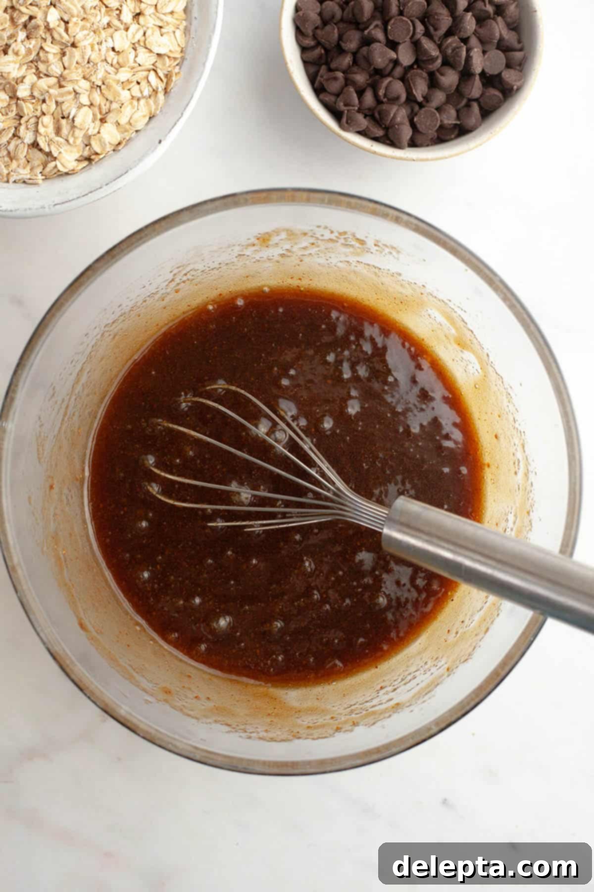 Irresistible Chewy Brown Butter Oatmeal Chocolate Chip Cookies 6 A glass bowl with a whisk and a dark brown liquid mixture of sugars, molasses, and vanilla in cooled brown butter.