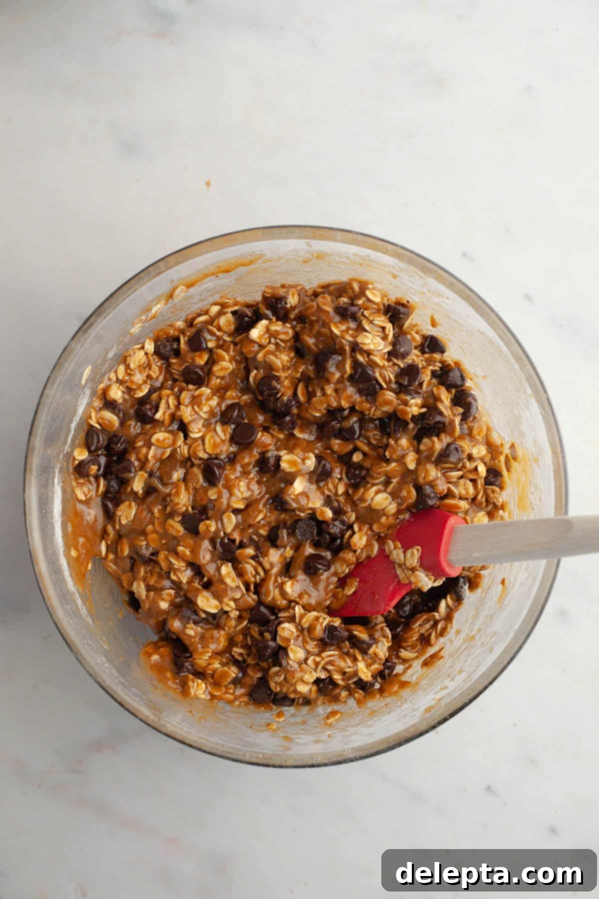 Irresistible Chewy Brown Butter Oatmeal Chocolate Chip Cookies 8 A glass bowl with oatmeal chocolate chip cookie dough, after oats and chocolate chips have been folded in.