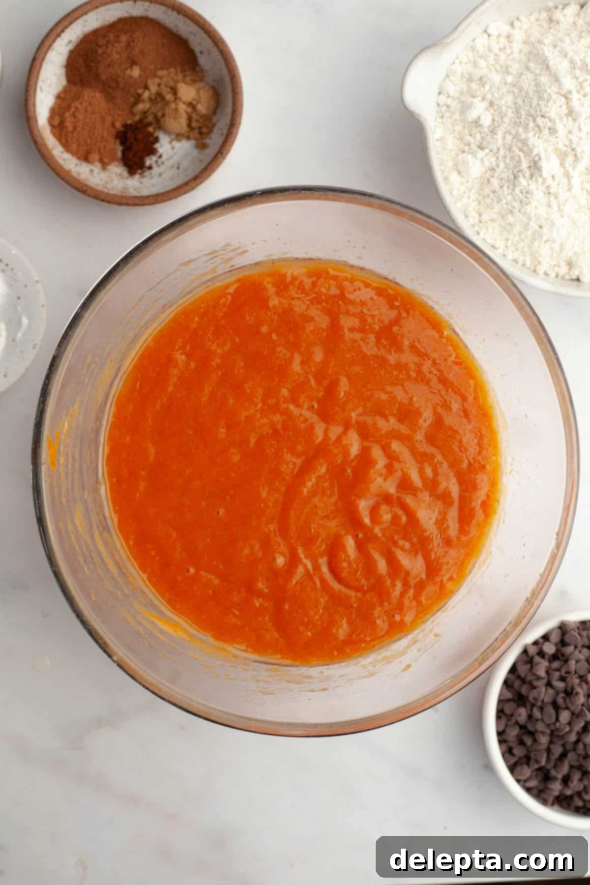 Cozy Mini Pumpkin Chocolate Chip Muffins 4 Pumpkin muffin batter in a clear glass bowl, showcasing its smooth, orange hue.