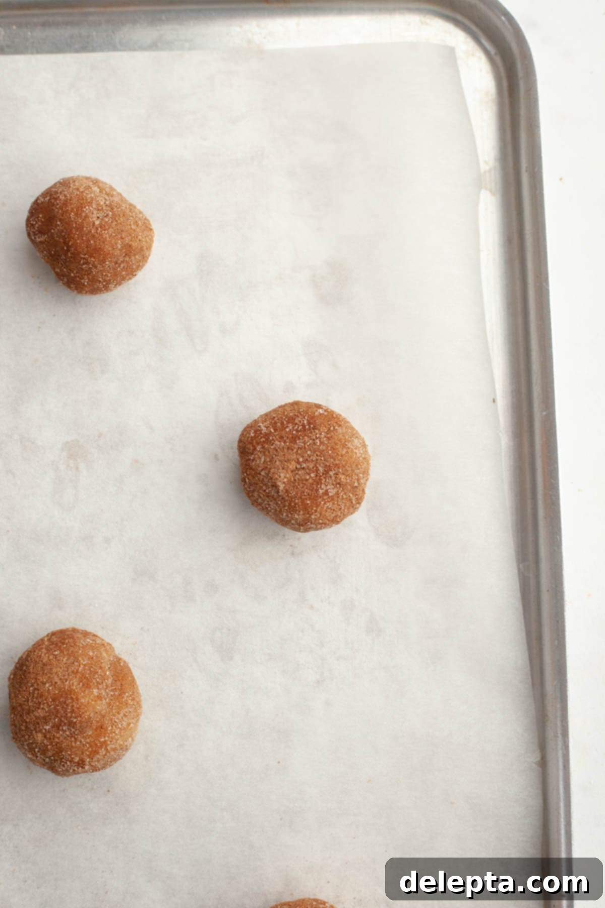 Ultimate Soft and Chewy Pumpkin Cookies 9 Unbaked pumpkin cookie dough balls rolled in pumpkin spice sugar on a parchment-lined baking sheet.