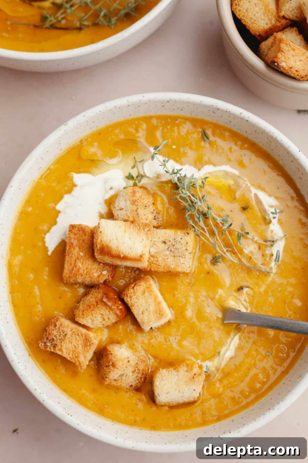 Warm Roasted Butternut & Carrot Ginger Soup 11 A white bowl with roasted carrot butternut squash soup and brioche croutons.