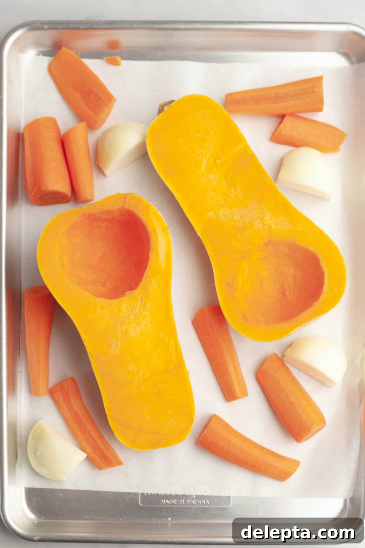 Warm Roasted Butternut & Carrot Ginger Soup 4 A sheet tray with chopped carrots, chopped onions and a butternut squash sliced in half.