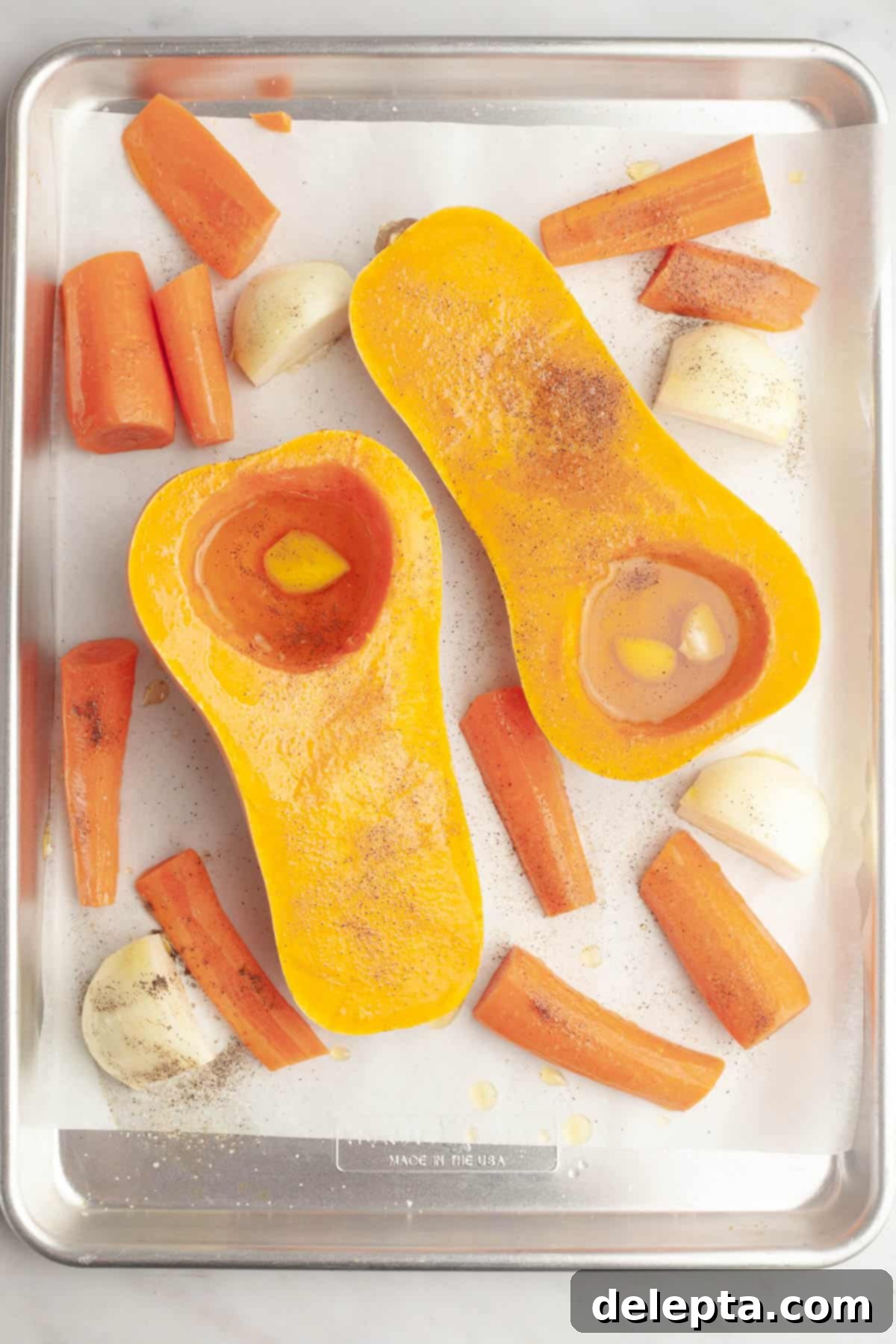 Warm Roasted Butternut & Carrot Ginger Soup 5 A sheet tray with chopped carrots, chopped onions and a butternut squash sliced in half.