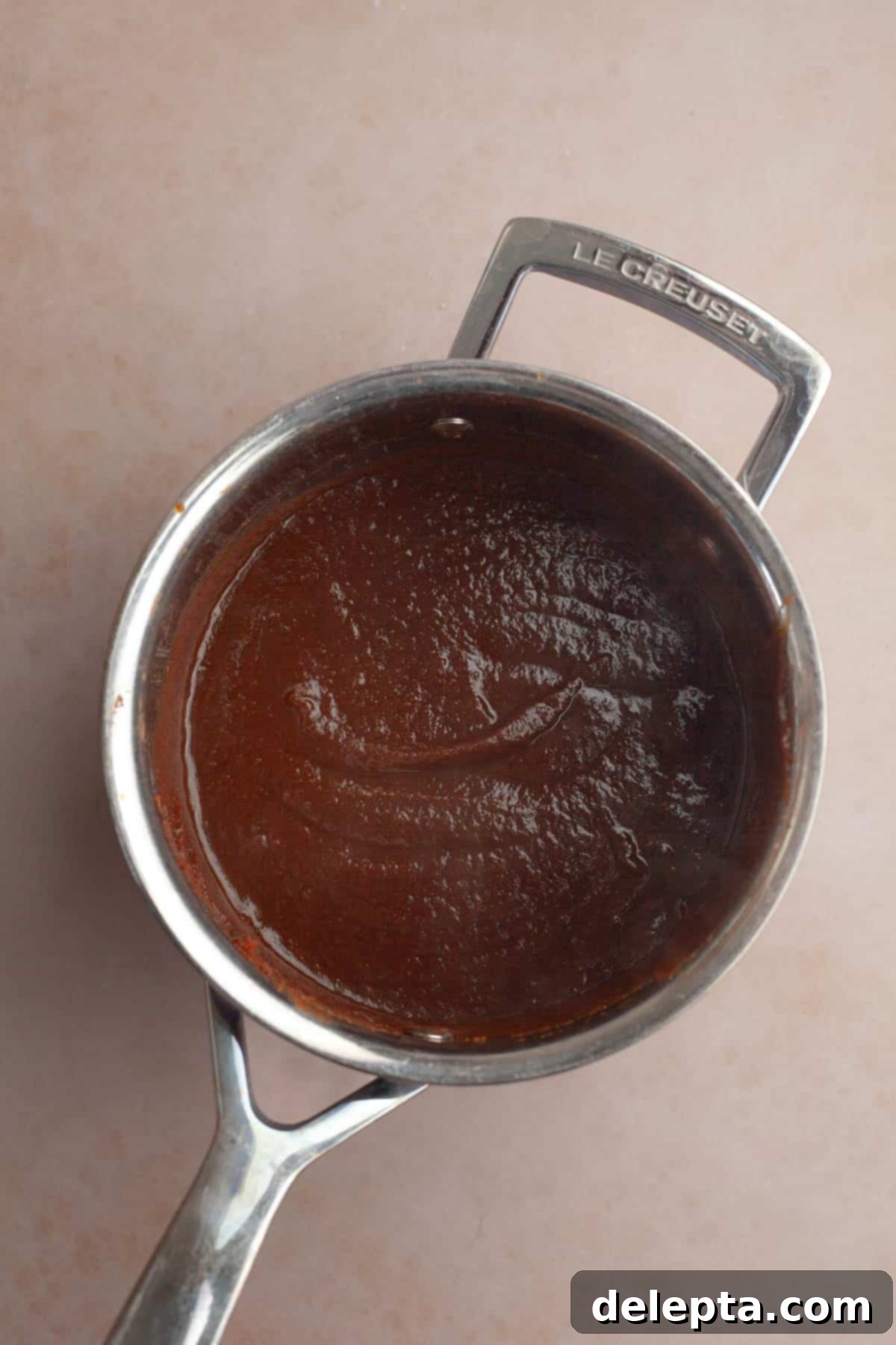 Easy Homemade Pumpkin Spice Syrup 5 A silver saucepan containing pumpkin sauce for coffee, gently simmering on the stove.