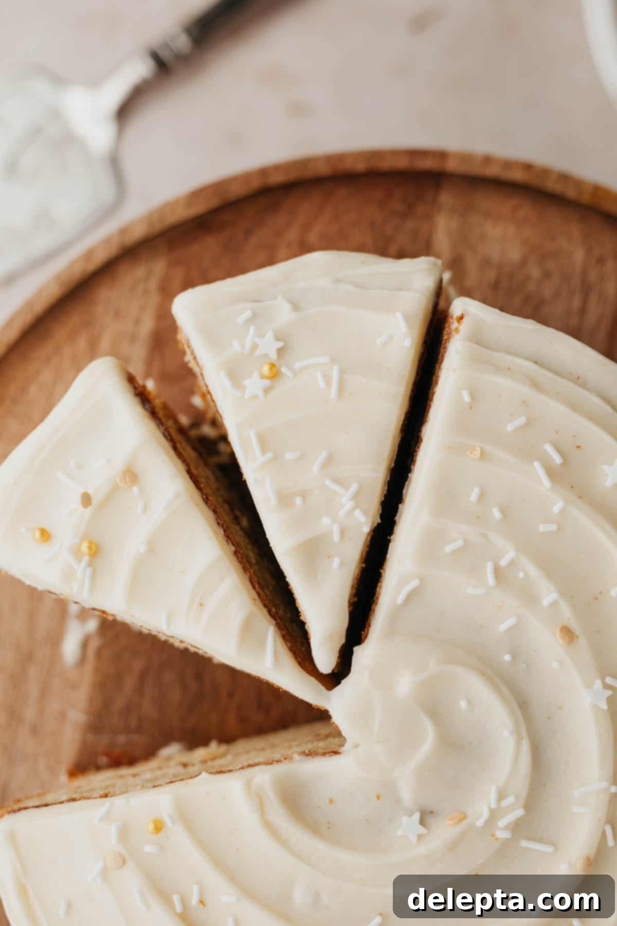 Brown Butter Cream Cheese Cardamom Cake 9 An overhead shot of a beautifully frosted cardamom cake with white frosting and delicate white sprinkles, with two perfect slices already cut.