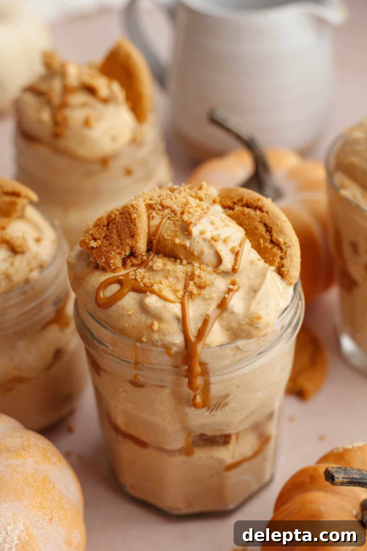 Effortless No Bake Pumpkin Delights 2 Individual pumpkin pie cups in mason jars, beautifully topped with crushed gingersnap cookies and a generous drizzle of golden cookie butter. A perfect no-bake fall dessert.