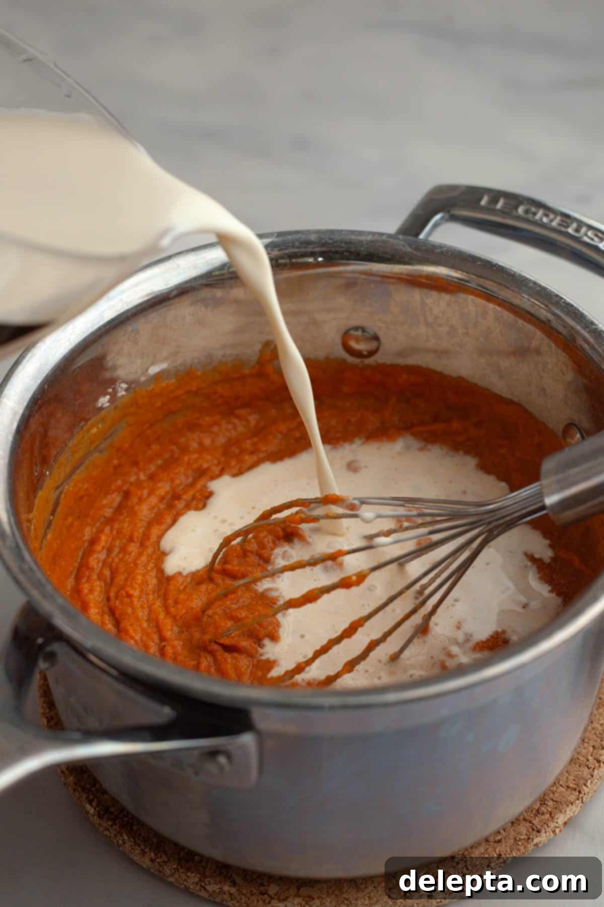 Effortless No Bake Pumpkin Delights 5 Heavy cream and whole milk being slowly drizzled into the pumpkin pudding mixture in a saucepan, being continuously whisked.