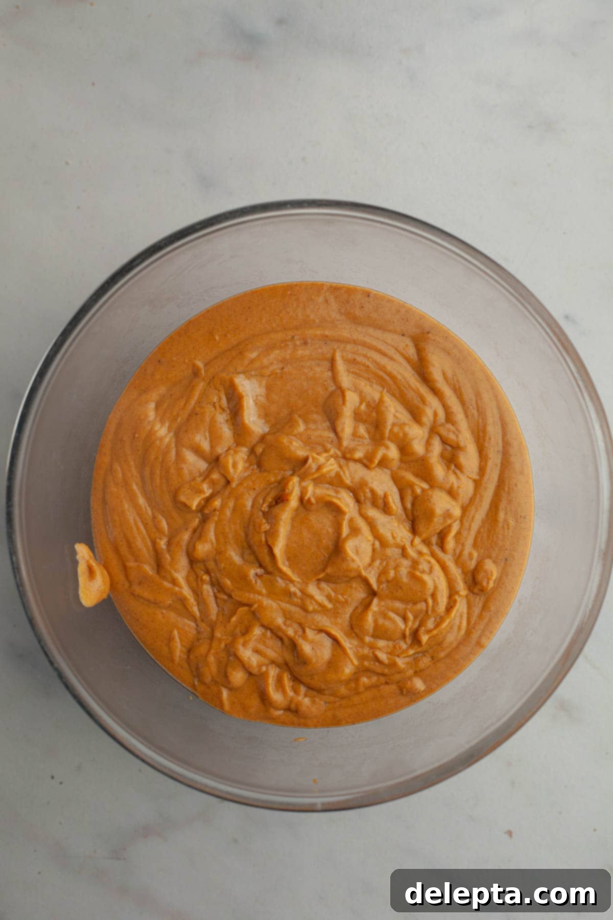 Effortless No Bake Pumpkin Delights 8 Thick, smooth pumpkin pudding poured into a large glass bowl, with plastic wrap pressed directly onto its surface to prevent a skin from forming.