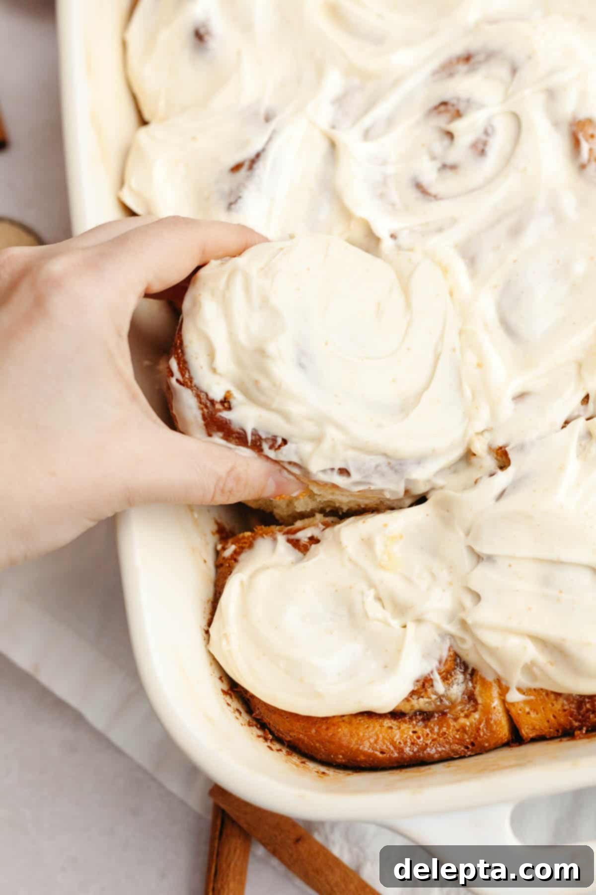 Rich Brown Butter Cinnamon Rolls with Velvety Brown Butter Frosting 15 A hand grabbing a brown butter cinnamon roll covered in cream cheese icing.