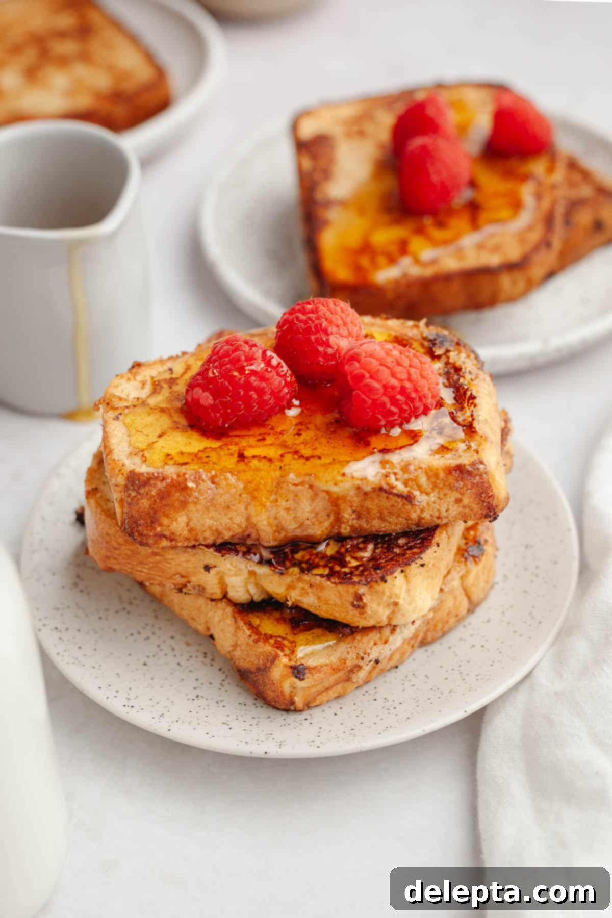 Effortless Buttermilk Brioche French Toast 11 Three slices of homemade buttermilk french toast presented on a small plate, beautifully garnished with fresh raspberries for a vibrant touch.