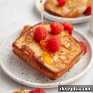Effortless Buttermilk Brioche French Toast 12 Two slices of fluffy buttermilk french toast on a small plate with fresh raspberries and luscious maple syrup being poured on top.