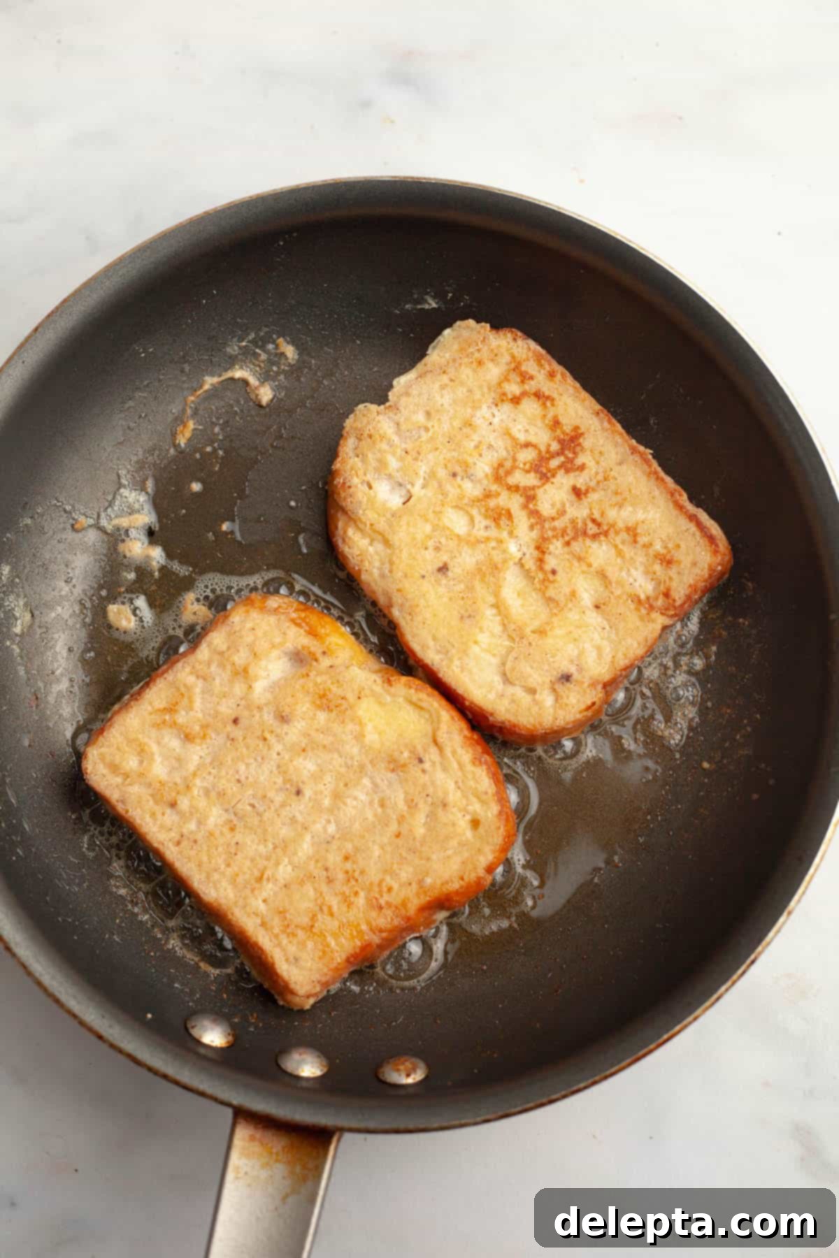 Effortless Buttermilk Brioche French Toast 7 A non-stick skillet with two slices of buttermilk french toast being cooked to golden perfection.