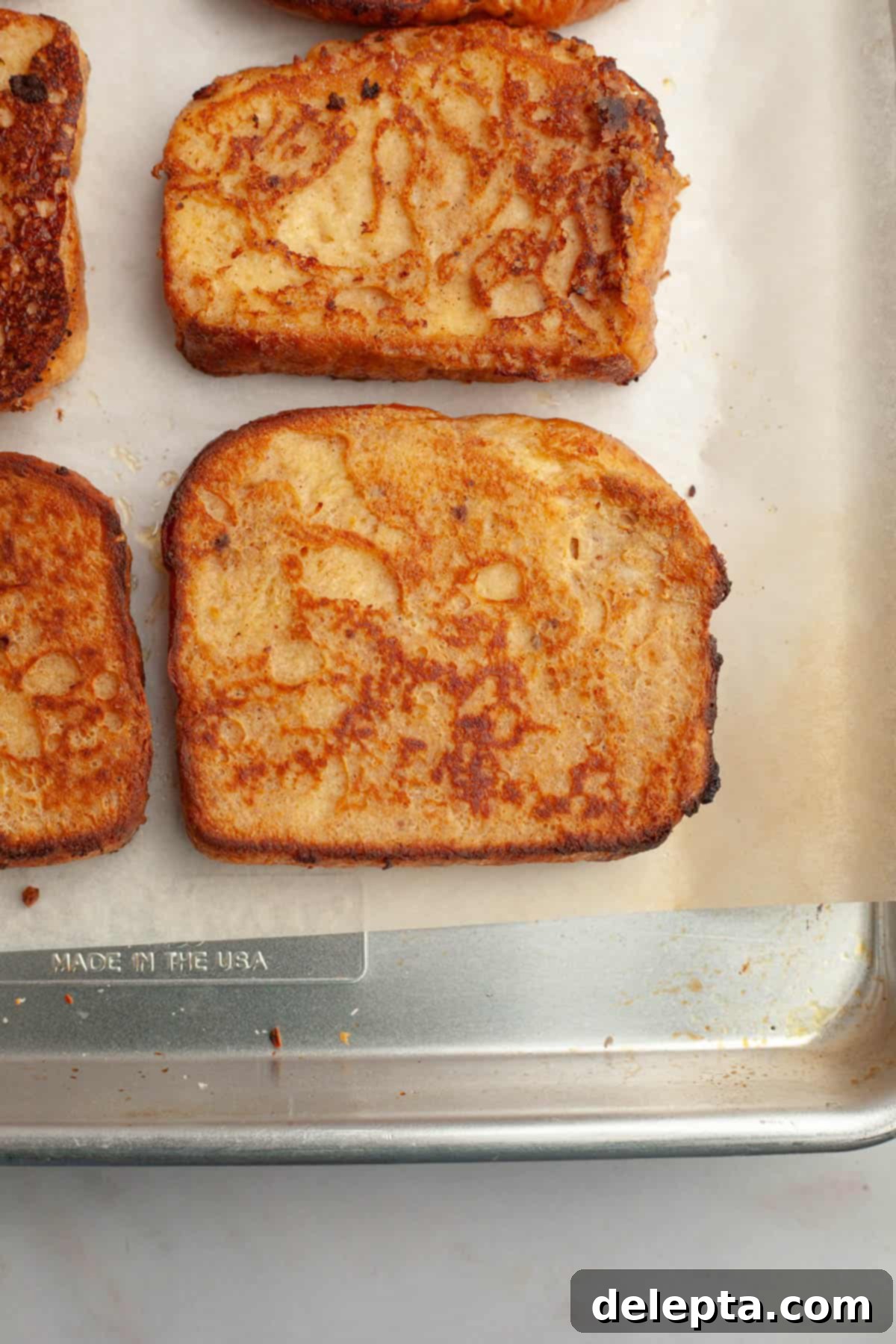 Effortless Buttermilk Brioche French Toast 8 Multiple slices of freshly cooked buttermilk french toast resting on a parchment-lined baking sheet in the oven, keeping warm.