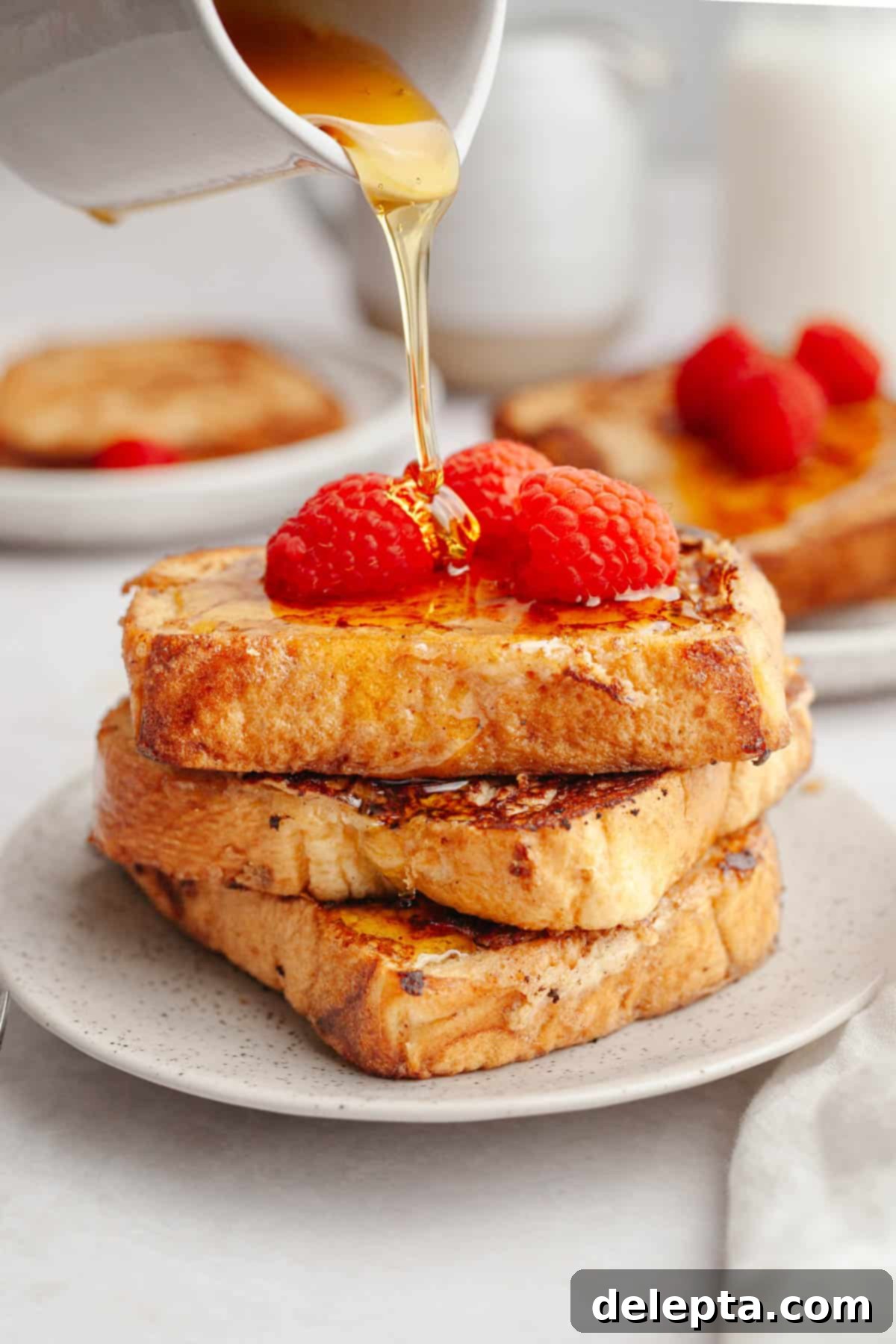 Effortless Buttermilk Brioche French Toast 9 Three slices of homemade buttermilk french toast on a small plate, generously topped with fresh raspberries and glistening maple syrup being poured over.