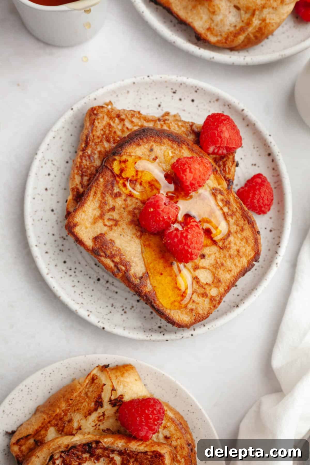 Effortless Buttermilk Brioche French Toast 10 Two golden slices of homemade buttermilk french toast artfully arranged on a small plate, adorned with vibrant fresh raspberries.