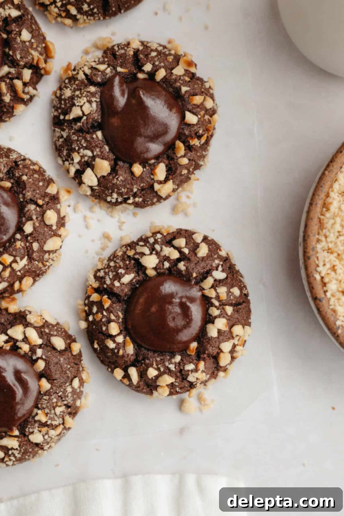 Double Nutella Bliss: Easy Thumbprint Cookies with Ganache 2 Nutella thumbprint cookies covered in chopped hazelnuts, showcasing their appealing texture and rich color.