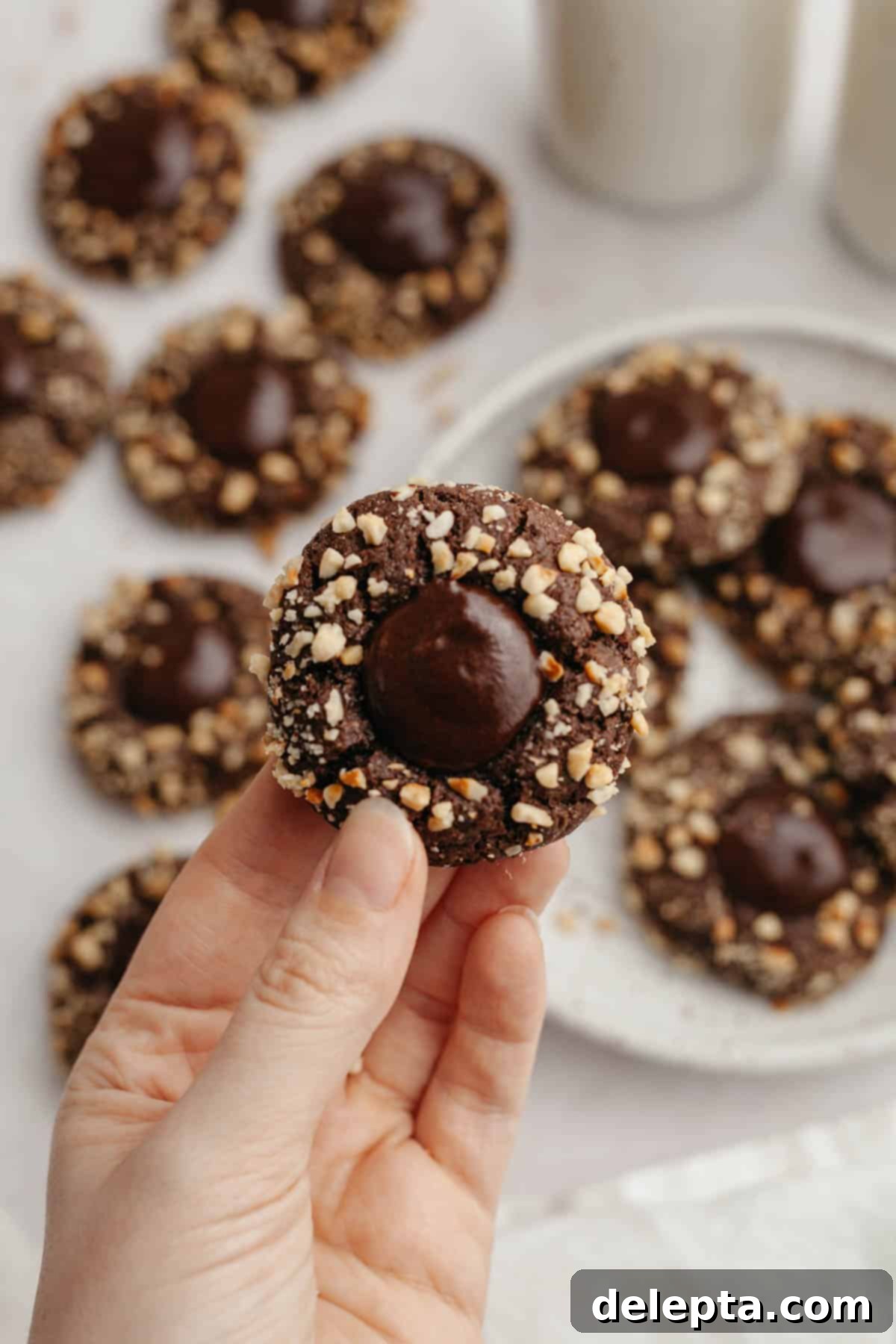 Double Nutella Bliss: Easy Thumbprint Cookies with Ganache 13 A hand holding a freshly baked Nutella thumbprint cookie, showcasing the ganache filling and hazelnut coating.