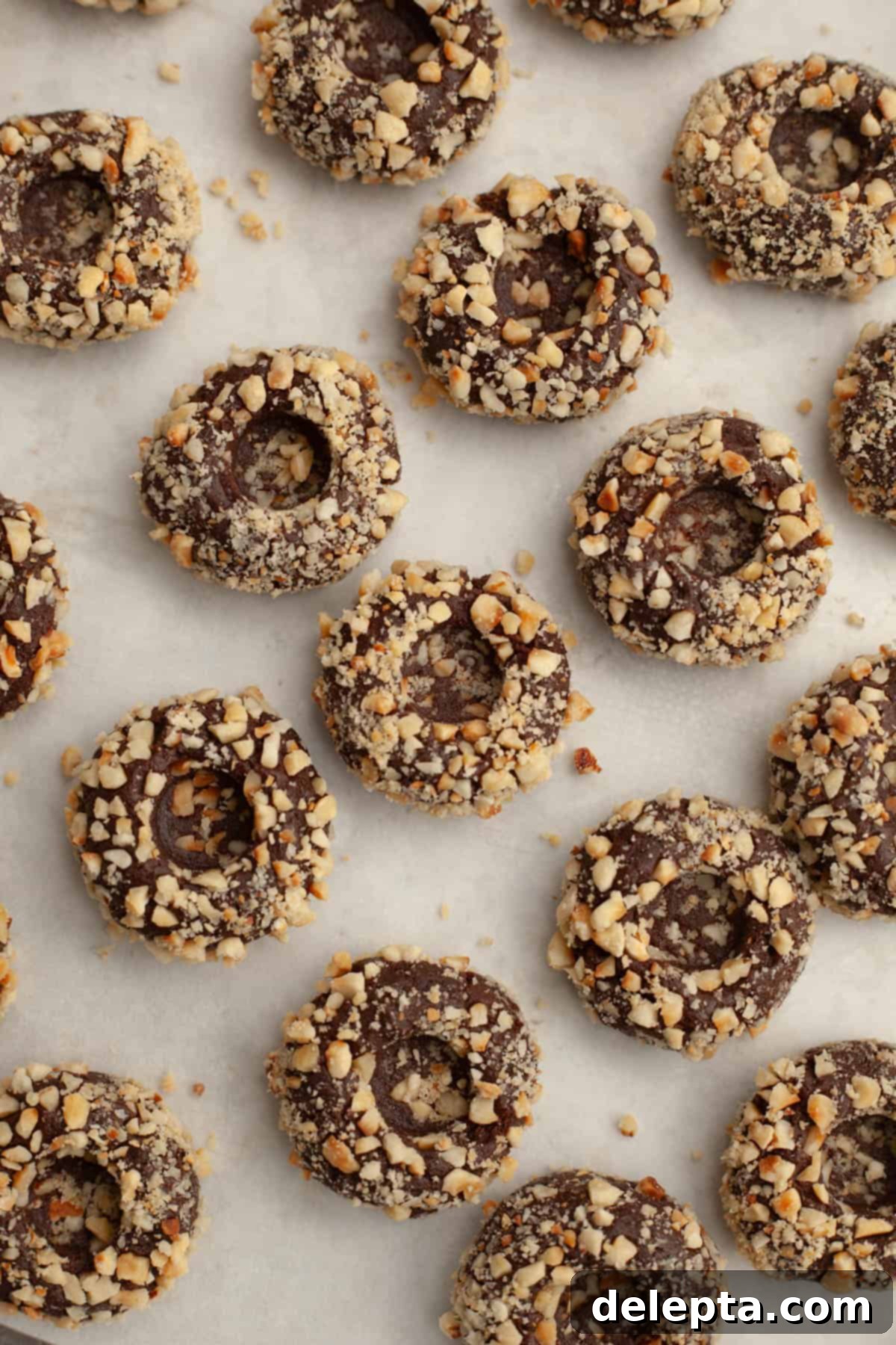 Double Nutella Bliss: Easy Thumbprint Cookies with Ganache 9 Chocolate cookie dough balls with indents, rolled in chopped hazelnuts, on a baking sheet, ready for chilling.