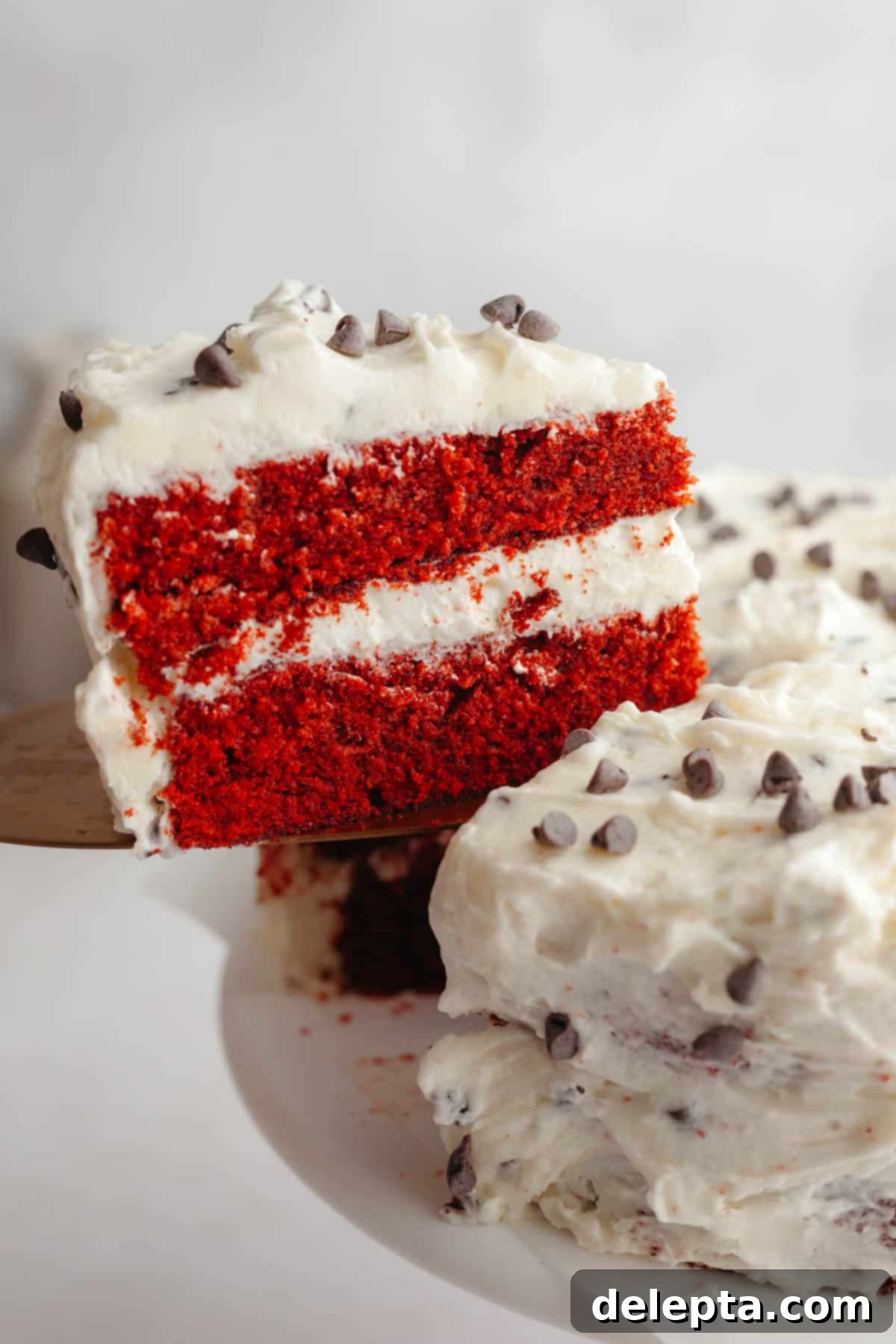 Red Velvet Chocolate Chip Indulgence 12 A delectable slice of red velvet chocolate chip cake, with its vibrant red layers and rich cream cheese frosting, being carefully lifted from the main cake.